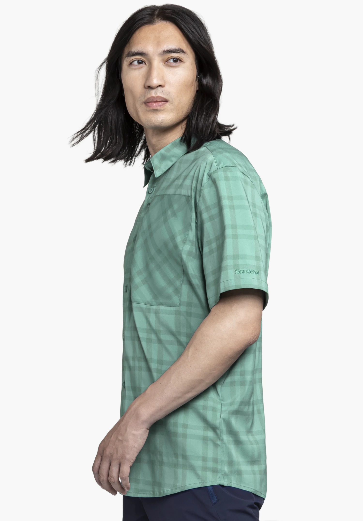 Shirt Style Frolya MEN in green. The model is standing sideways, showcasing the short-sleeved checked shirt with the Schöffel logo on the sleeve against a neutral background.