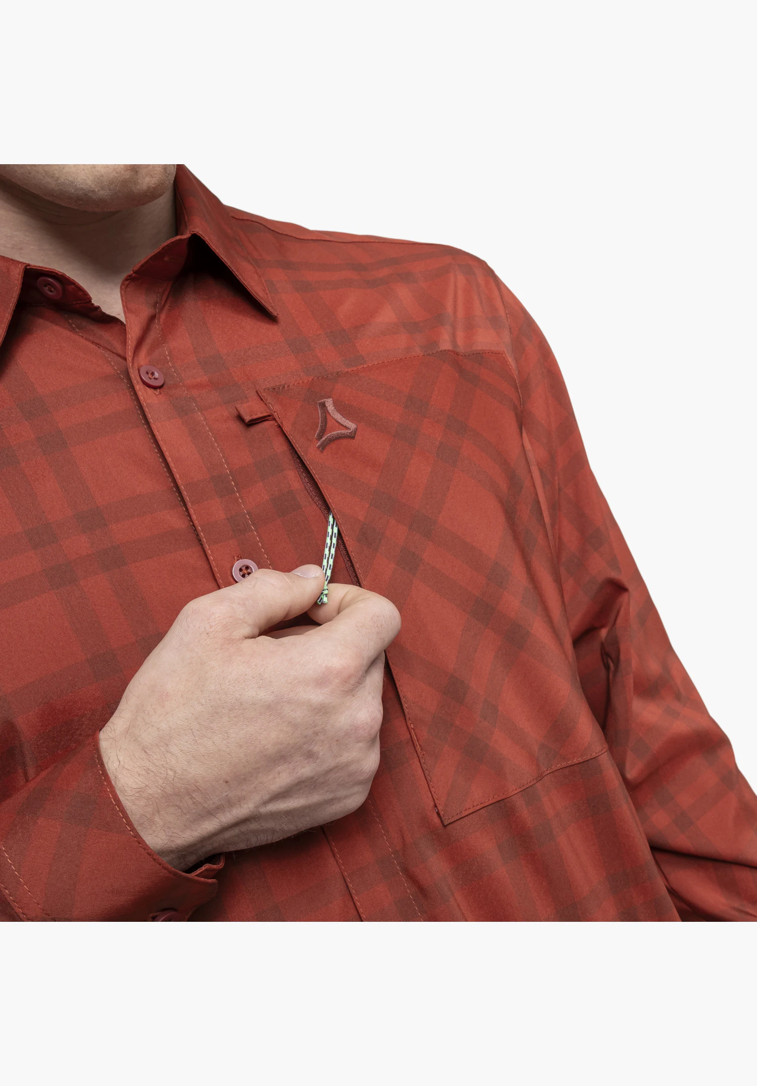 Shirt Style Fraris MEN shown in detail on the red chest area with a checked pattern. A hand operates the pull cord of the discreet chest pocket zip, with the colour-coordinated Schöffel logo placed above it, close-up against a white background.