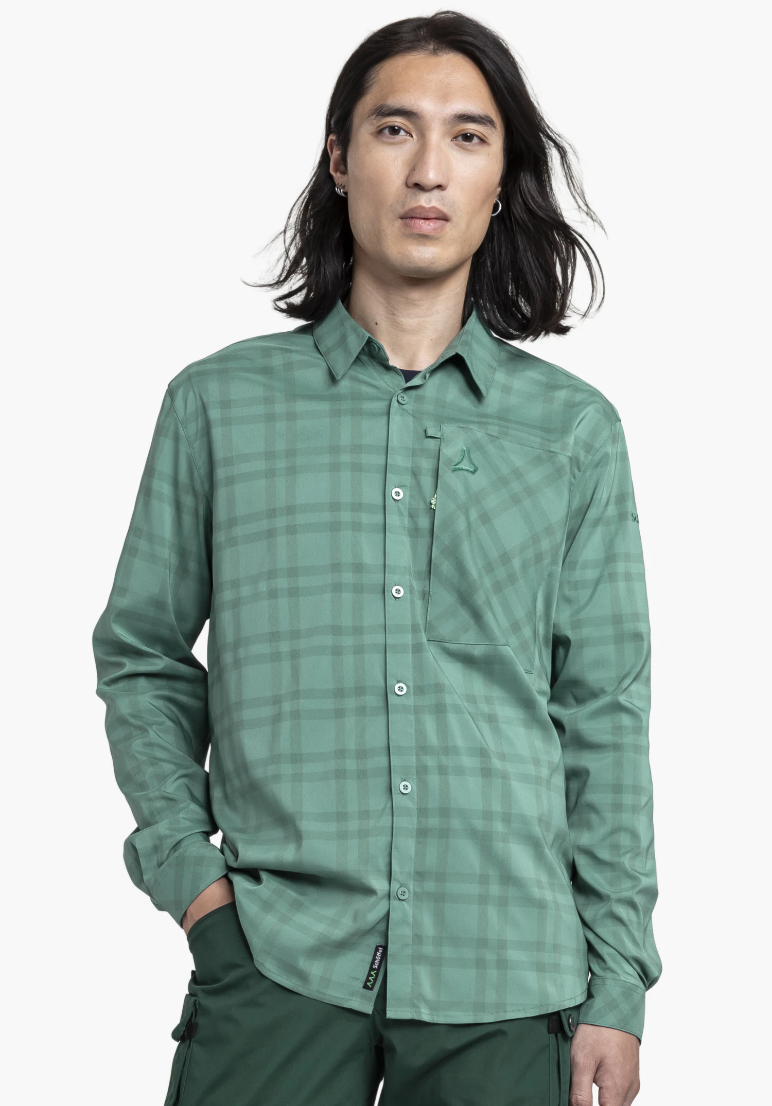 Shirt Style Fraris MEN in Grün, präsentiert von einem Model in Frontalansicht vor einem neutralen Hintergrund. Das Hemd überzeugt durch sein dezentes Karomuster, die Brusttasche mit dezentem Schöffel-Logo sowie ein weiteres Schöffel-Logo am unteren Saum.