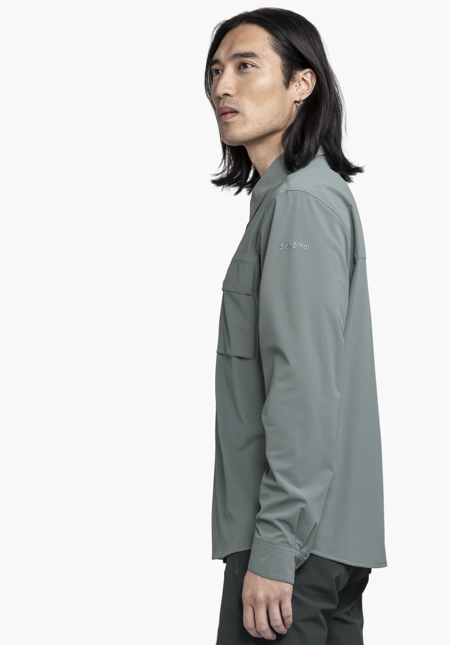 Shirt Style Dunajec MEN in grey. The male model is standing in profile against a neutral background, showcasing the shirt. The subtle Schöffel logo on the sleeve highlights the functional look for versatile outdoor activities.