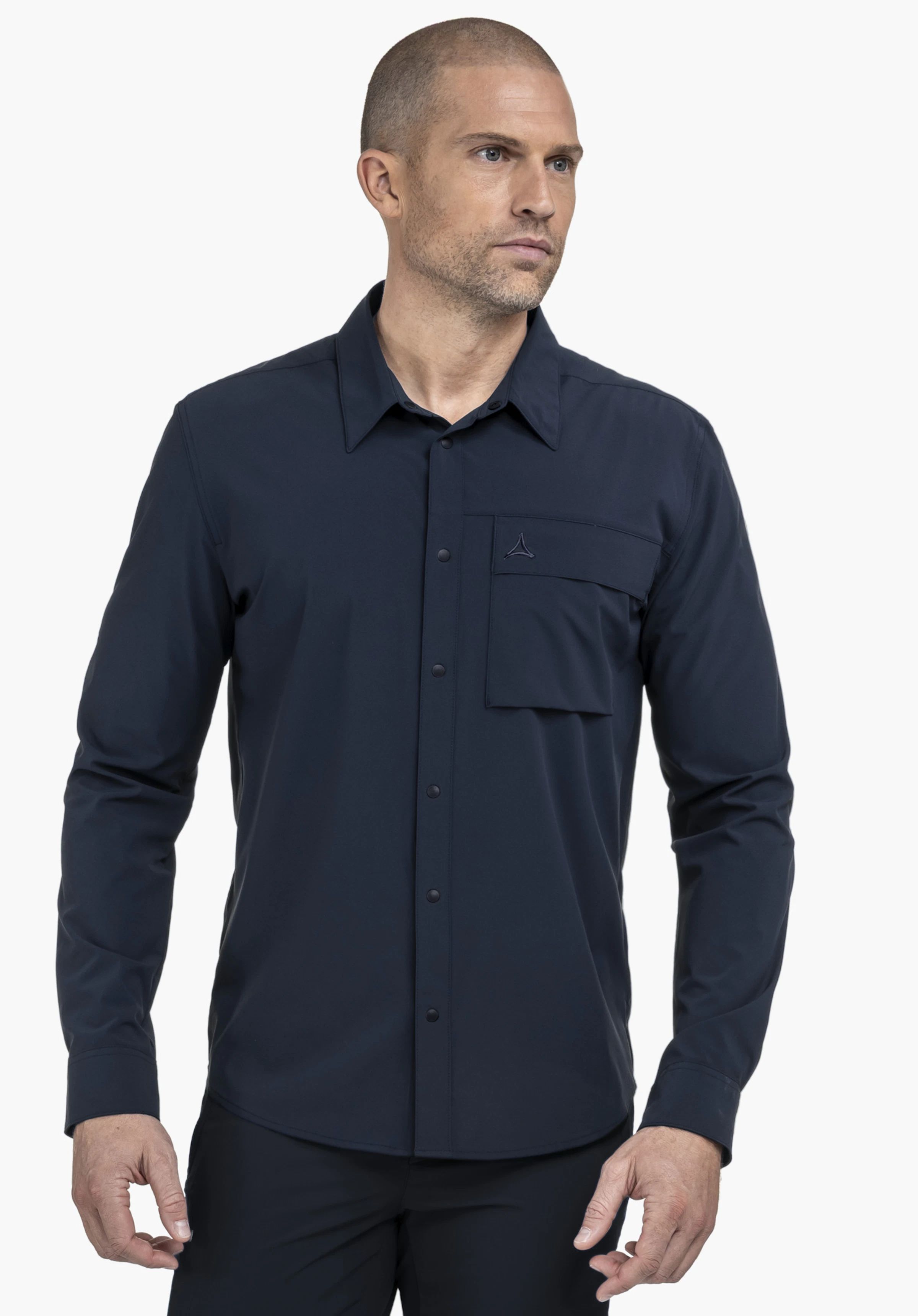 Shirt Style Dunajec MEN en bleu est présenté sur un mannequin masculin regardant vers l'avant. Posant sur un fond neutre, la chemise à manches longues arbore le logo Schöffel discret sur la poche poitrine.