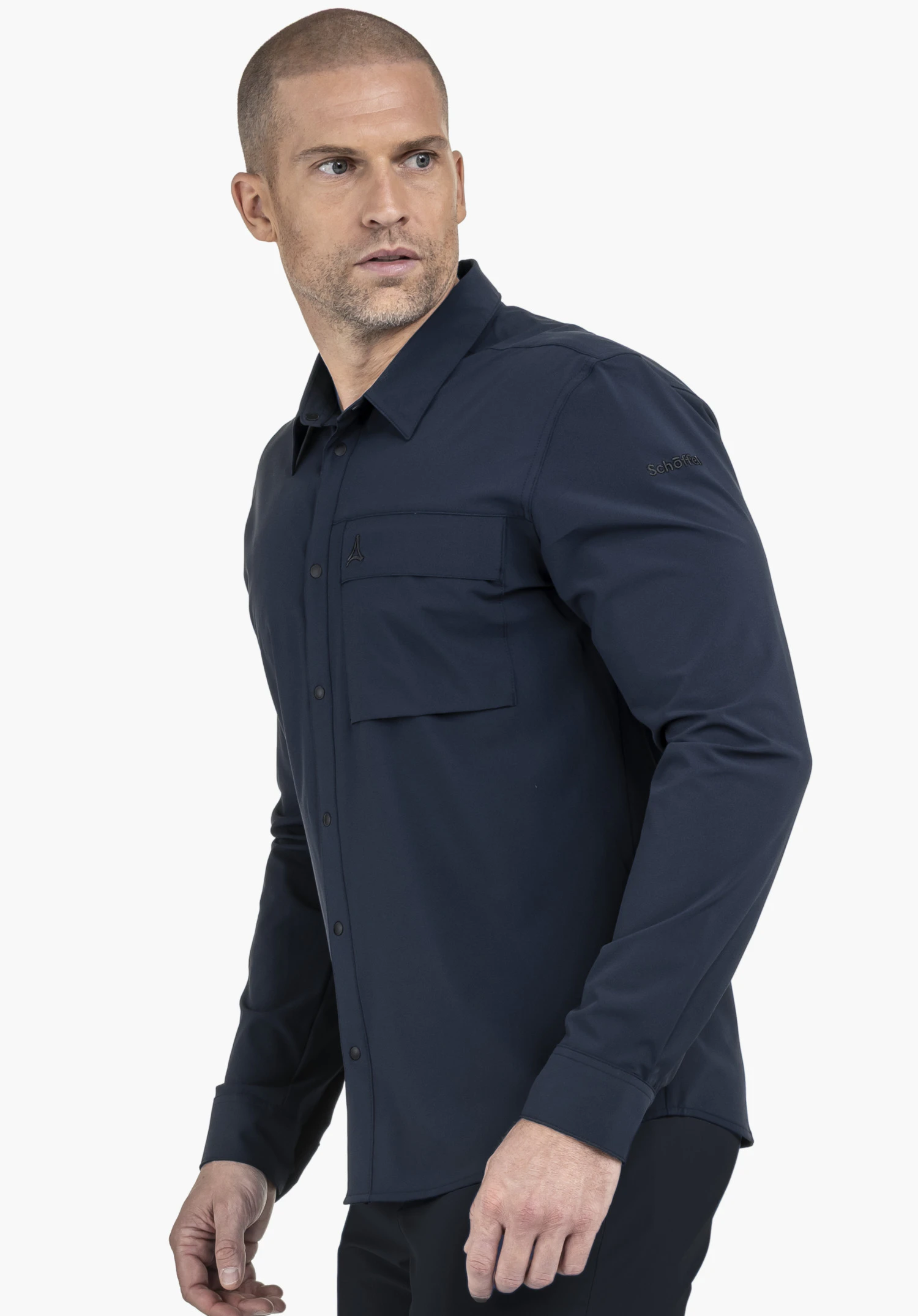 Shirt Style Dunajec MEN en bleu porté par un mannequin, photographié de profil alors qu'il détourne le regard. Sur un fond neutre, le design met en valeur la poche poitrine et le logo Schöffel discret situé sur le haut du bras.