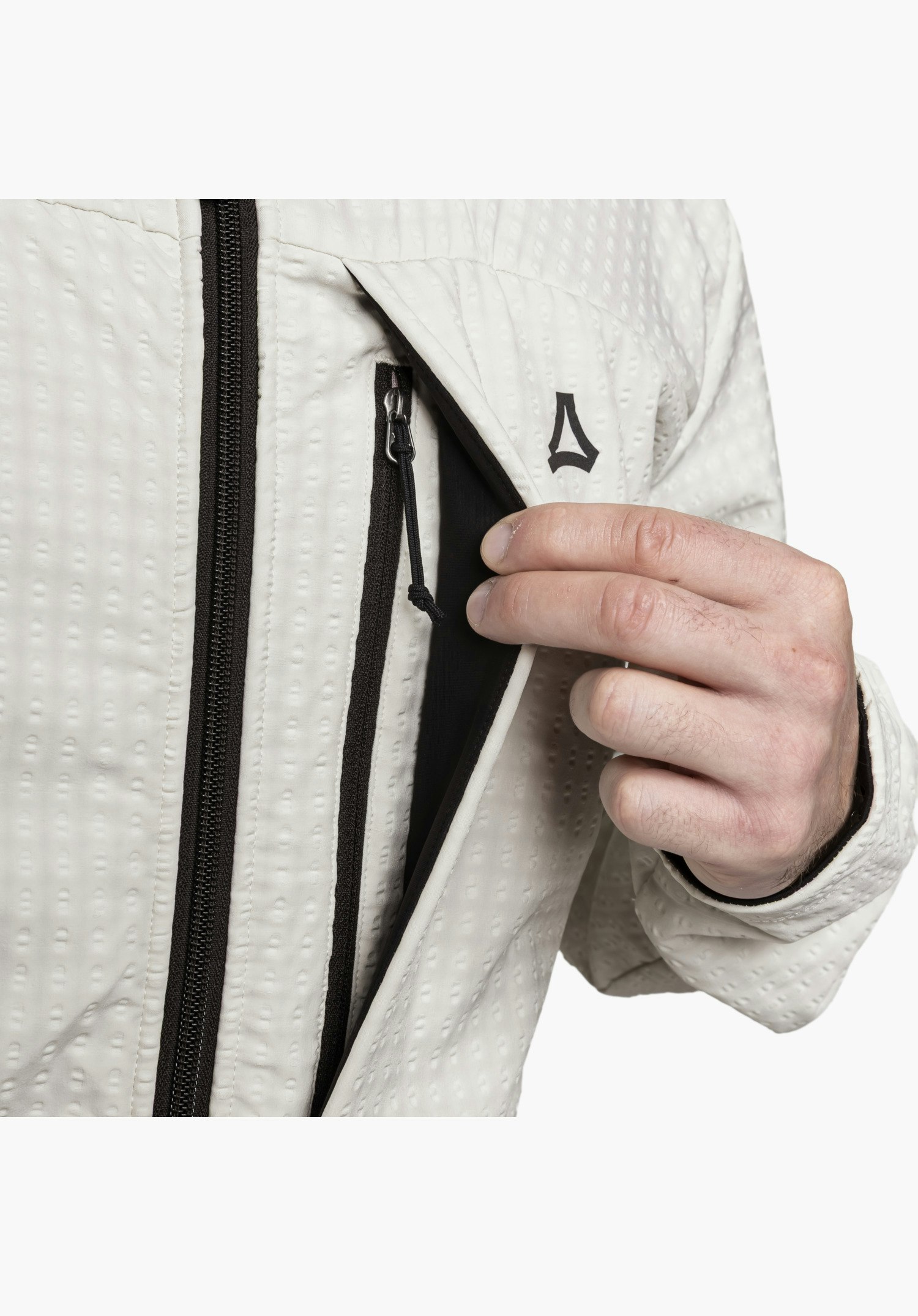 Fleece Hoody Style Enixa MEN zeigt im Detail eine von einer Hand geöffnete Brusttasche mit schwarzem Reißverschluss und das schwarze Schöffel-Logo auf dem strukturierten Fleece-Stoff in der Farbe Natur, Nahaufnahme vor weißem Hintergrund.
