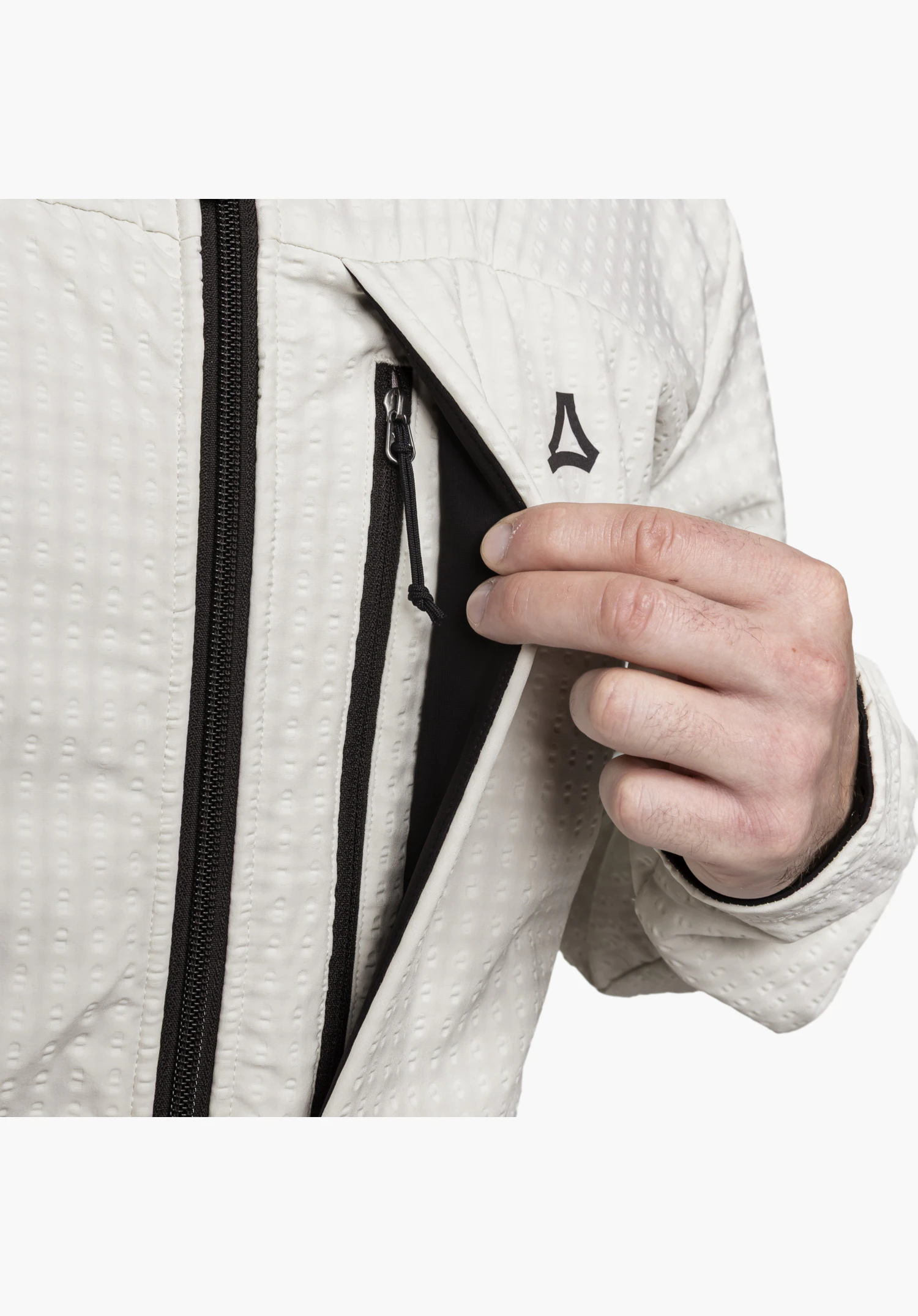 Fleece Hoody Style Enixa MEN showing a detail of an open chest pocket with a black zip held by a hand and the black Schöffel logo on the textured fleece fabric in the colour natur, close-up against a white background.