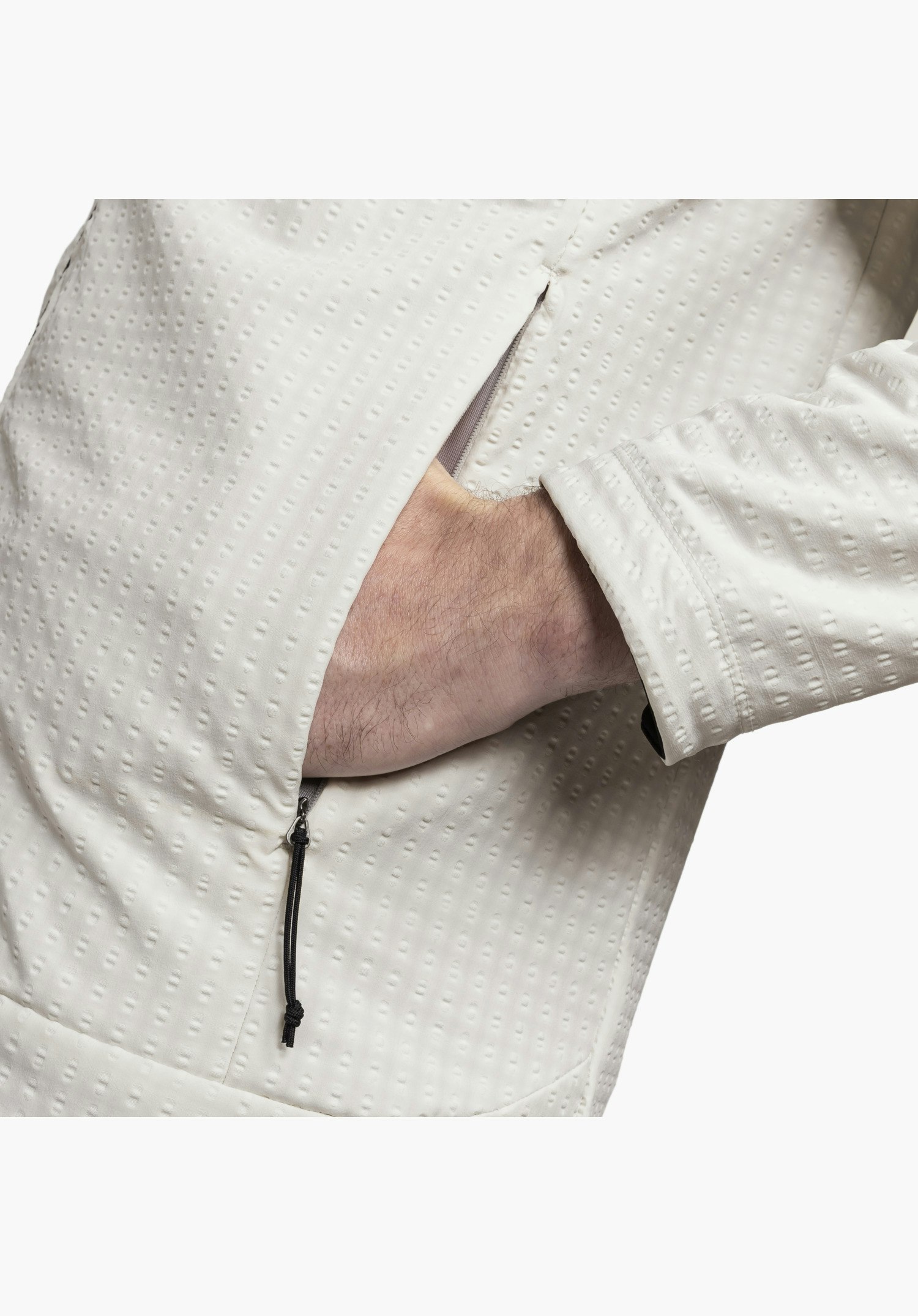 Fleece Hoody Style Enixa MEN, Fokus auf den strukturierten Fleece-Stoff in der Farbe Natur mit seinem markanten dreidimensionalen Muster und eine Hand in der seitlichen Reißverschlusstasche mit schwarzem Kordelzug, Nahaufnahme vor weißem/neutralem Hintergrund.