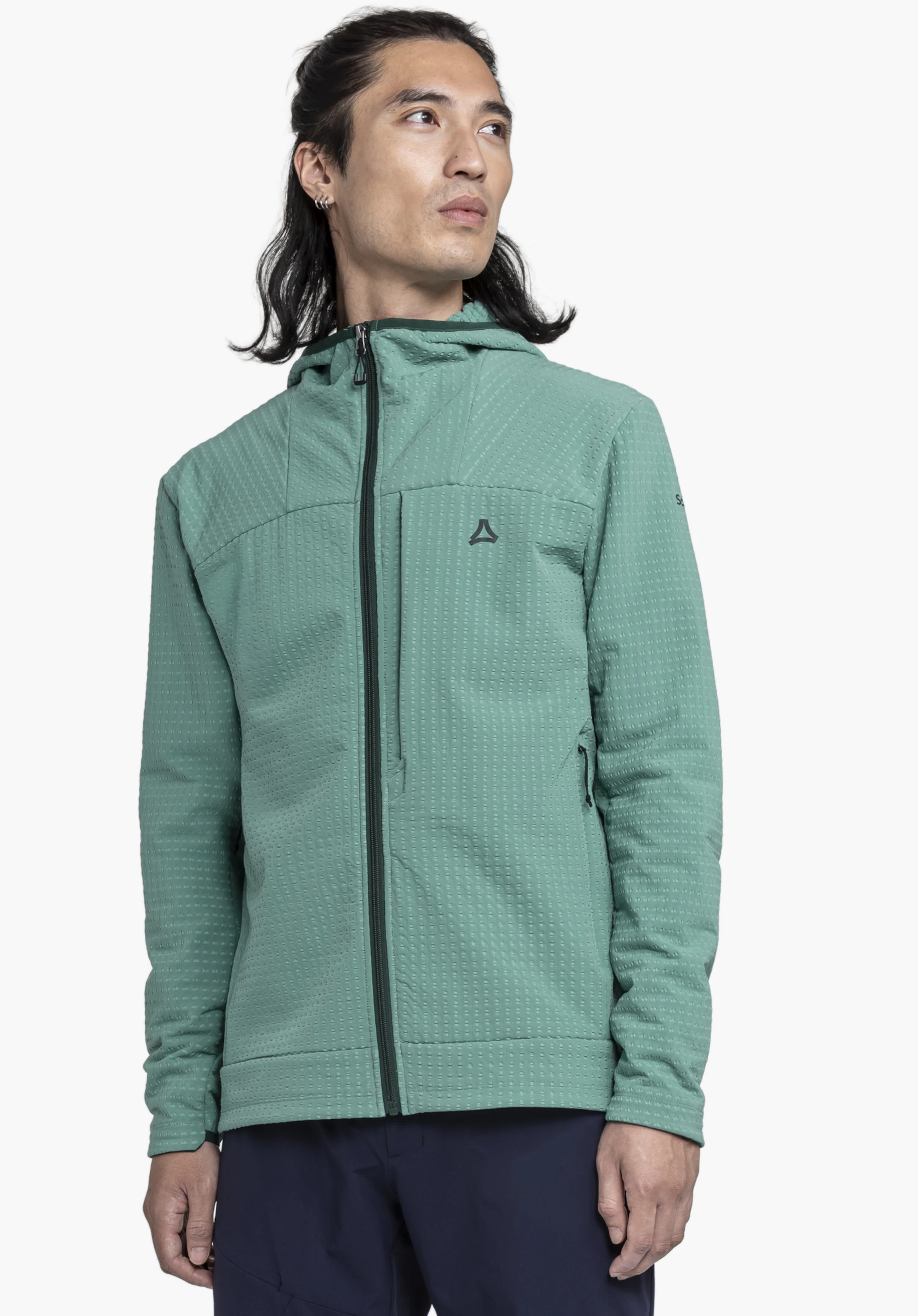 Fleece Hoody Style Enixa MEN. Un mannequin se tient de face, regarde sur le côté et présente le sweat à capuche vert avec le logo Schöffel bien visible sur la poitrine, devant un fond neutre.