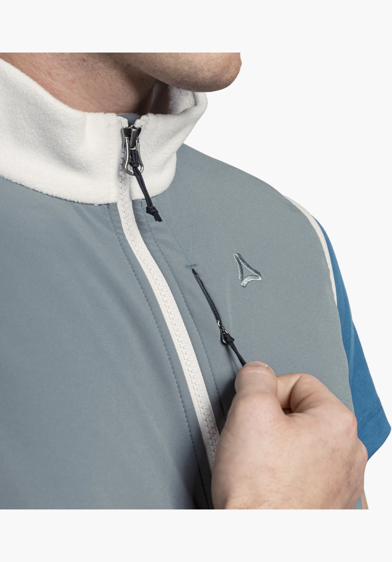 Fleece Vt Style Ash MEN shows the grey fabric detail on the chest featuring the embroidered Schöffel logo, a white front zip and a hand pulling the chest pocket zip, in a close-up against a white/neutral background.