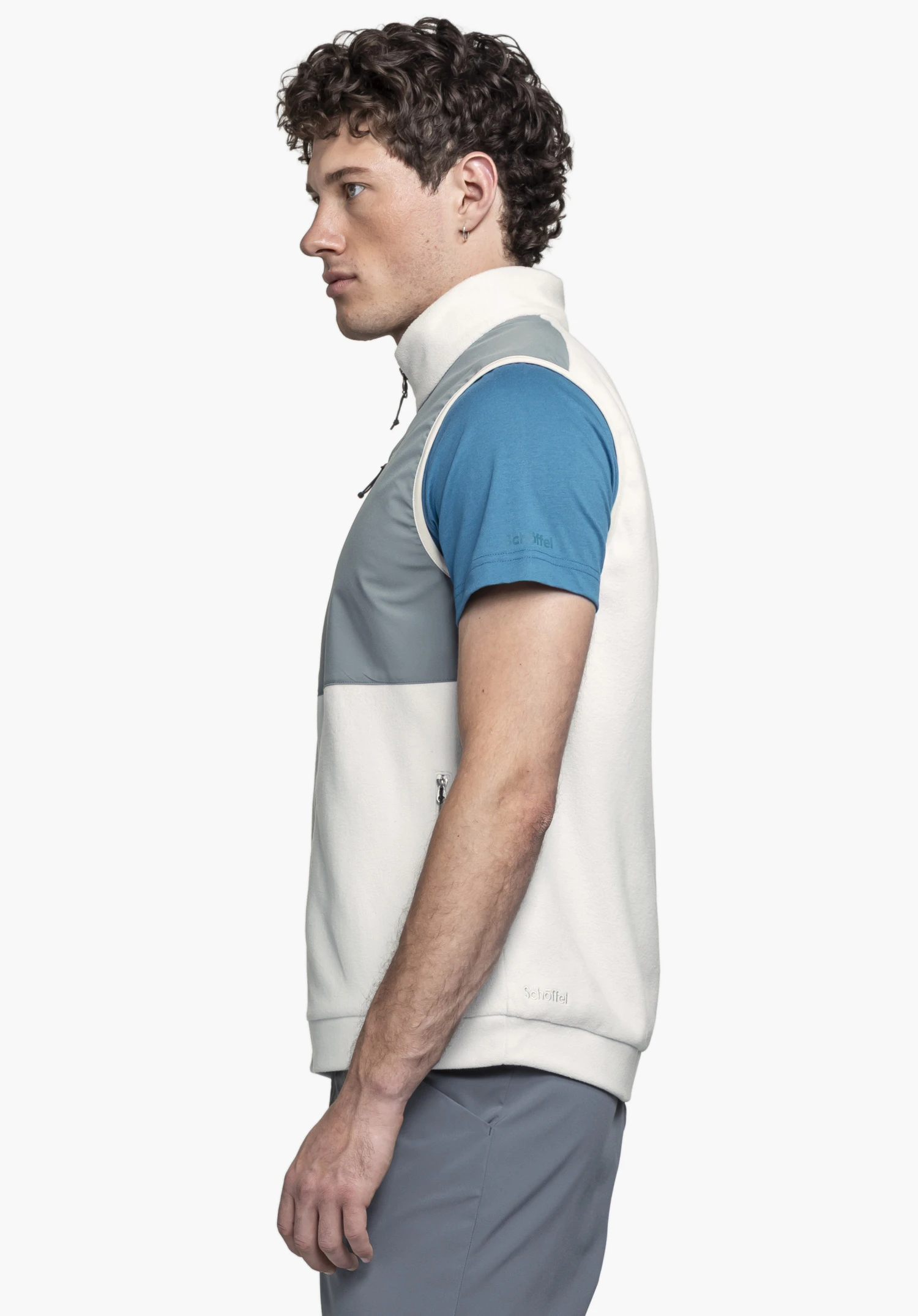 Fleece Vt Style Ash MEN in grey: A model stands sideways against a neutral background, showcasing the vest with its grey accents that complement the fit. The subtle Schöffel logo on the bottom hem highlights the premium design.