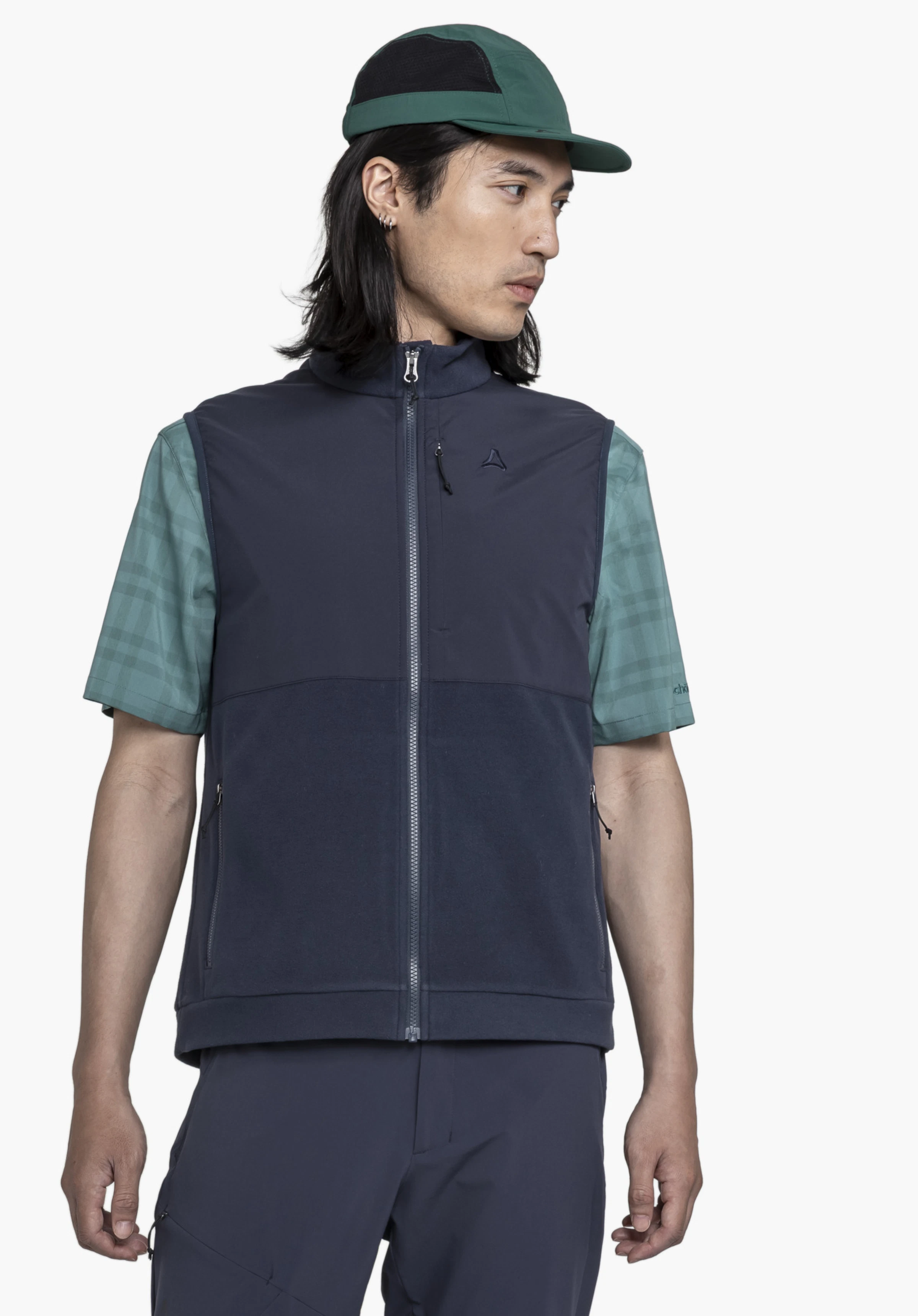 Fleece Vt Style Ash MEN an einem Model, das in Frontalansicht steht und zur Seite blickt. Die blaue Weste mit sichtbarem Schöffel-Logo auf der linken Brust wird über einem grünen Kurzarmhemd getragen, präsentiert vor einem neutralen Hintergrund.
