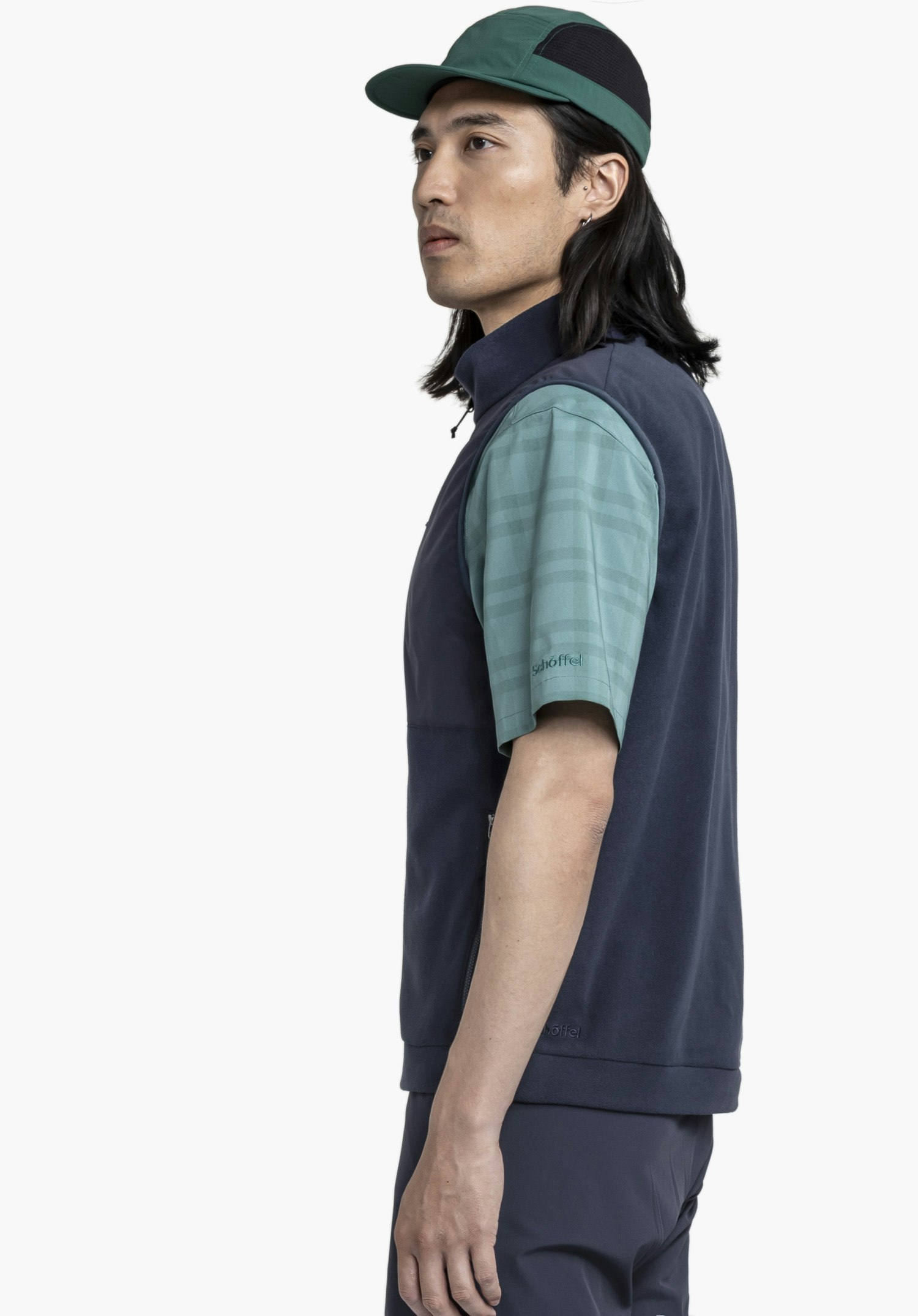 Fleece Vt Style Ash MEN in Blau. Ein Model steht seitlich vor einem neutralen Hintergrund und präsentiert die Weste, die das dezente Schöffel-Logo am Saum zeigt.