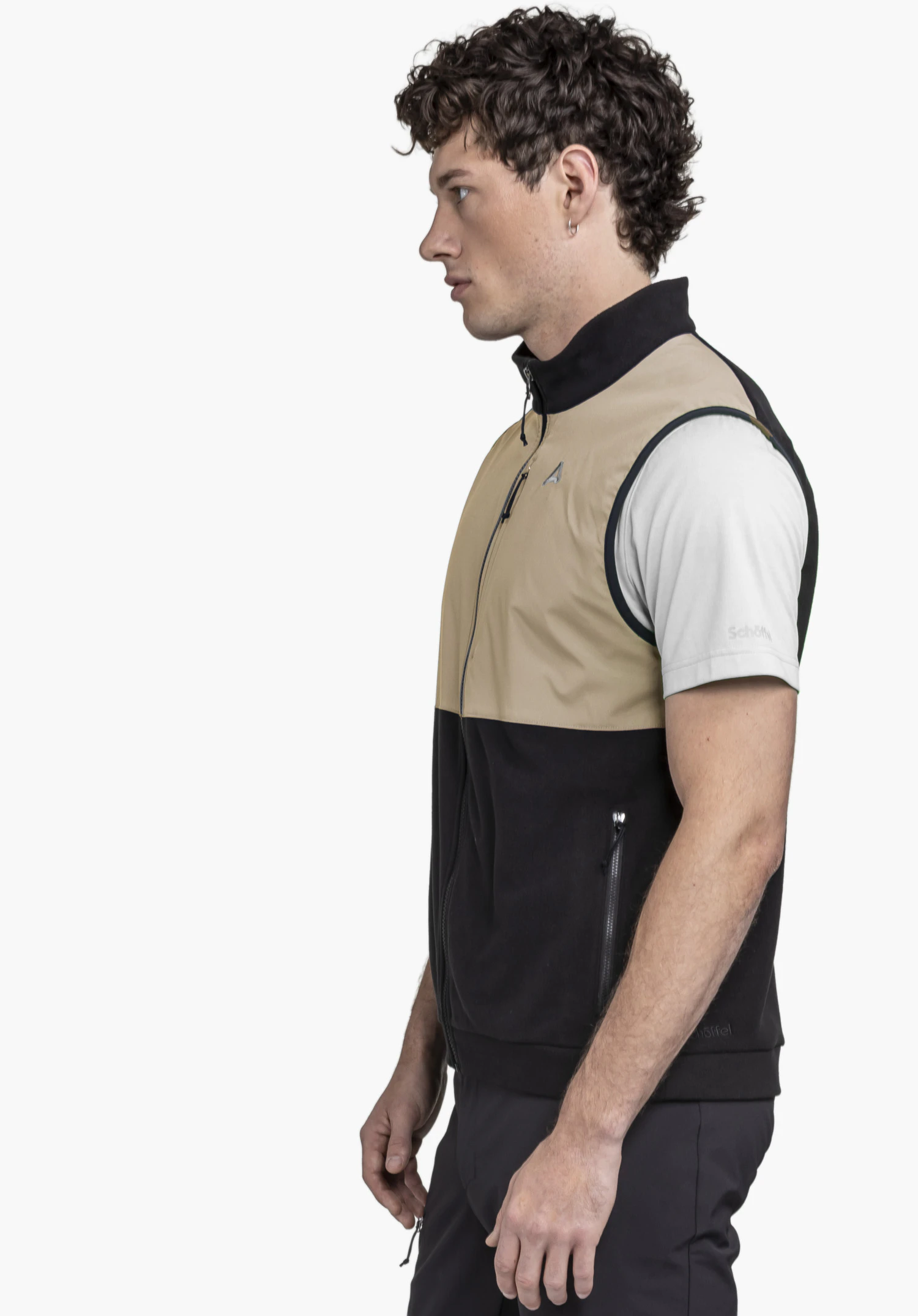 Fleece Vt Style Ash MEN is shown on a model from a side profile against a neutral background. The fleece vest combines a black lower section with a beige upper part and features the subtle Schöffel logo on the chest and hem.