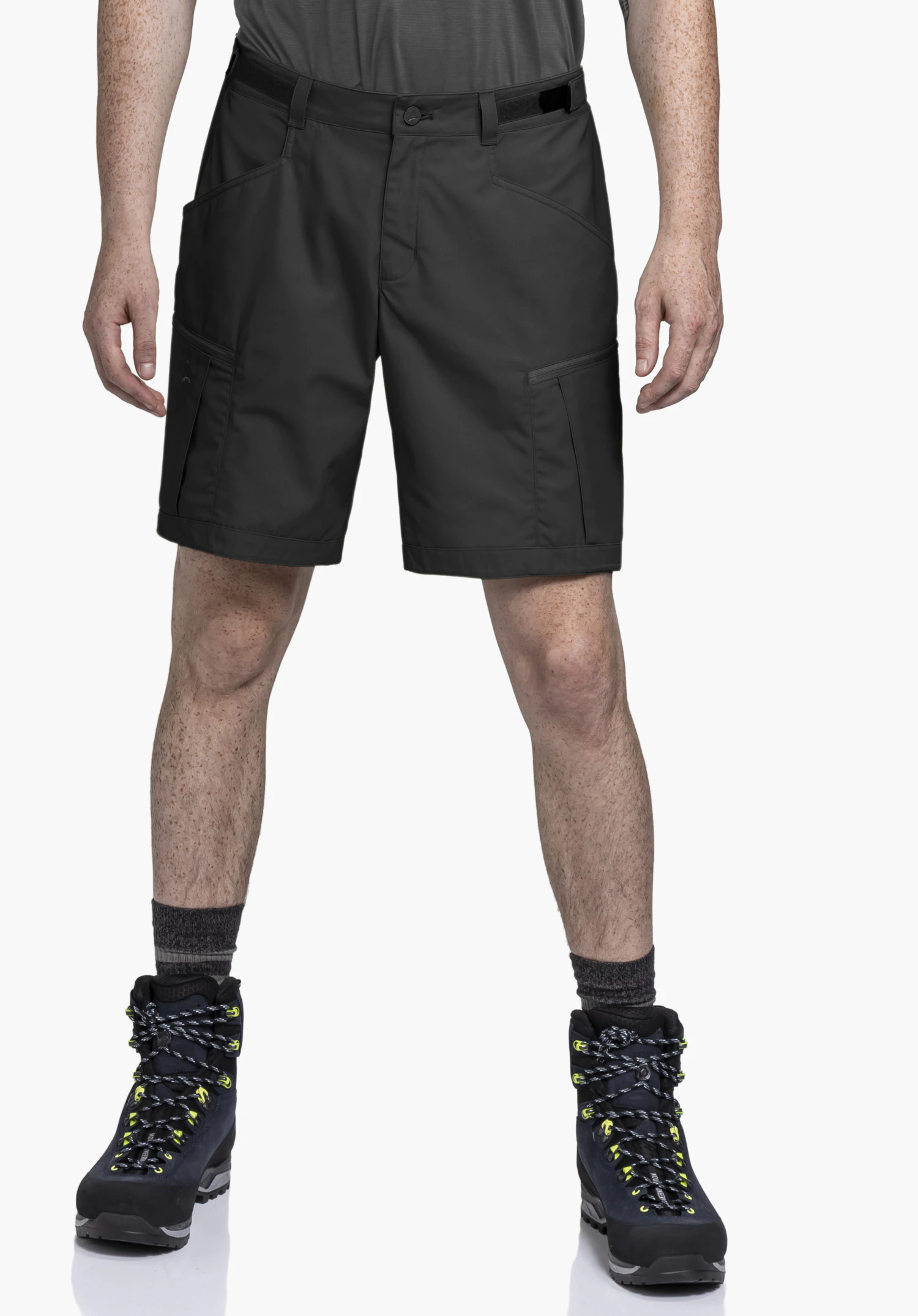 Shorts Style Maghera MEN in der Farbe Schwarz, getragen von einem Model. Das Model steht in Frontalansicht und kombiniert die Hose mit Wanderschuhen vor einem neutralen Hintergrund. Ein dezentes Schöffel-Logo ist auf der rechten Beintasche erkennbar.