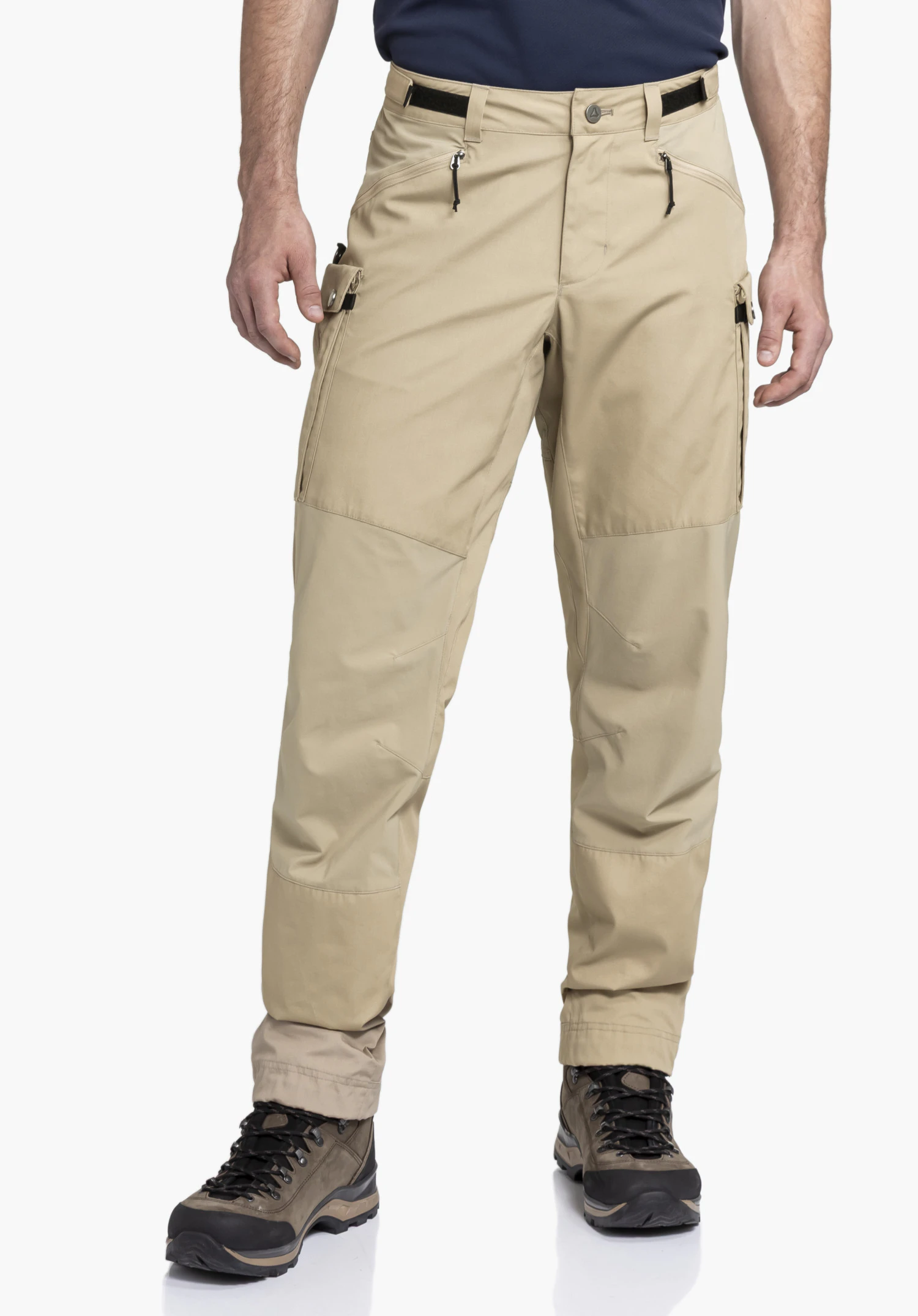 Pants Style Maghera MEN. A model stands frontally and presents the beige trekking trousers with side zip pockets. The worn view is shown against a neutral background together with hiking boots.