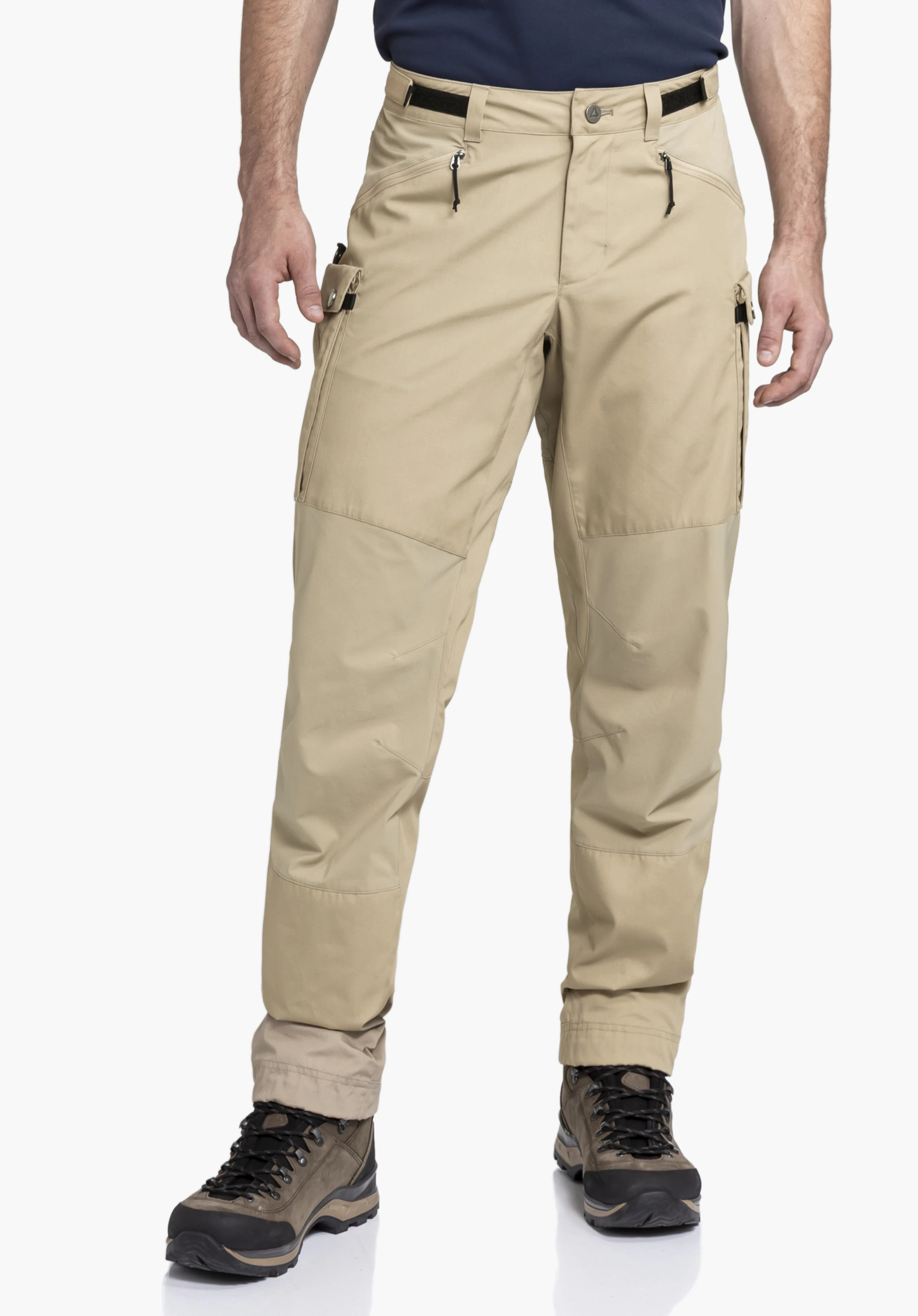 Pants Style Maghera MEN. A model stands frontally and presents the beige trekking trousers with side zip pockets. The worn view is shown against a neutral background together with hiking boots.