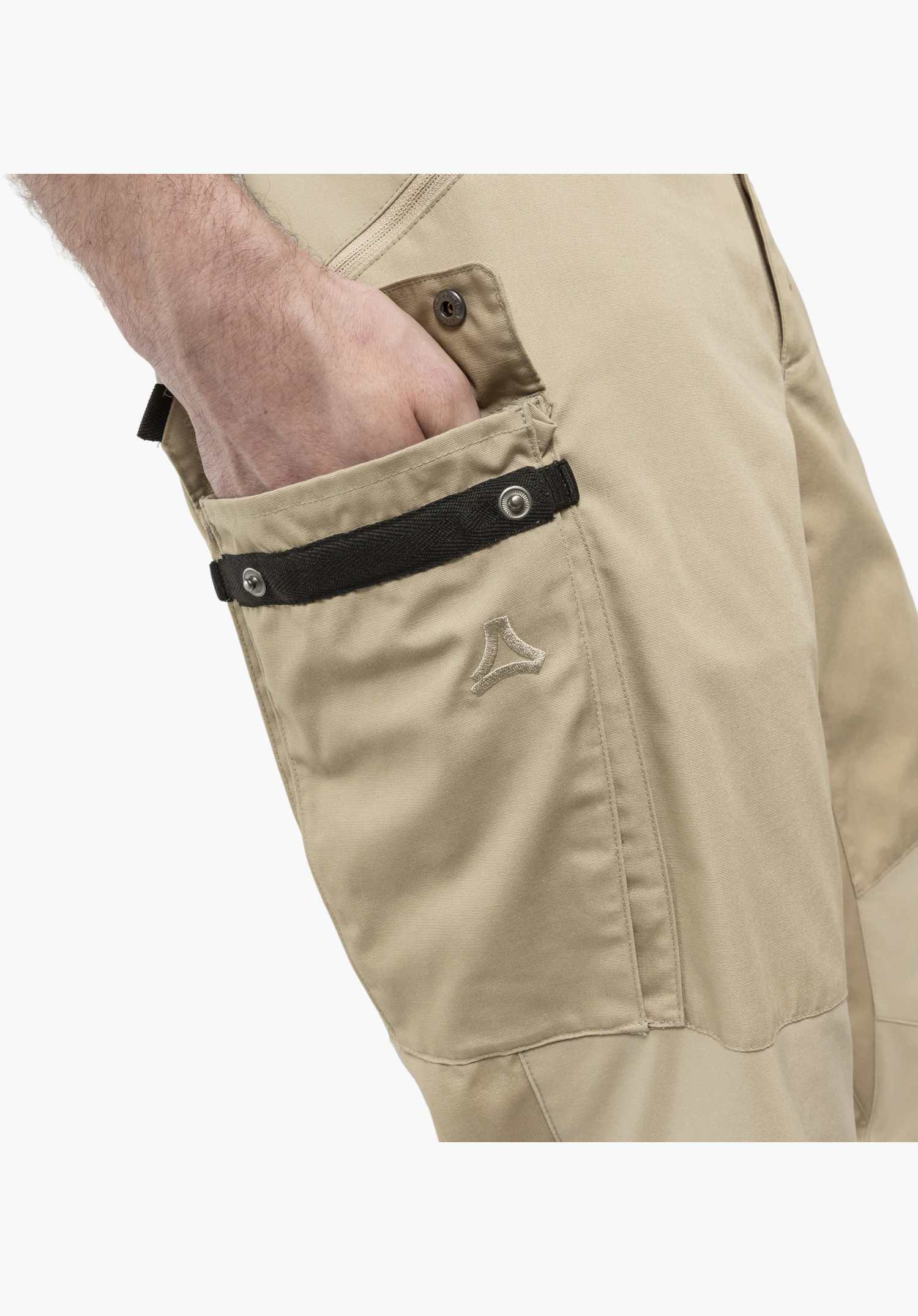 Pants Style Maghera MEN shows the beige leg pocket in detail featuring a black textile strap, metal snap buttons, the embroidered Schöffel logo and a hand in the upper slip pocket, close-up against a white background.