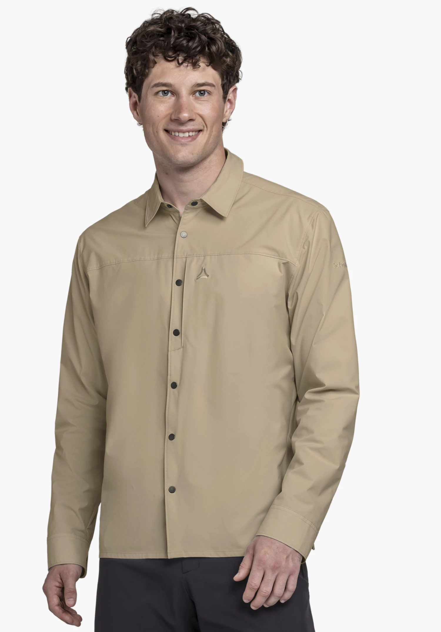 Shirt Style Maghera MEN als beigefarbenes Langarmhemd an einem lächelnden Model. Das Model steht leicht seitlich vor einem neutralen Hintergrund und präsentiert die dunkle Knopfleiste sowie das kleine Schöffel-Logo auf der linken Brust.