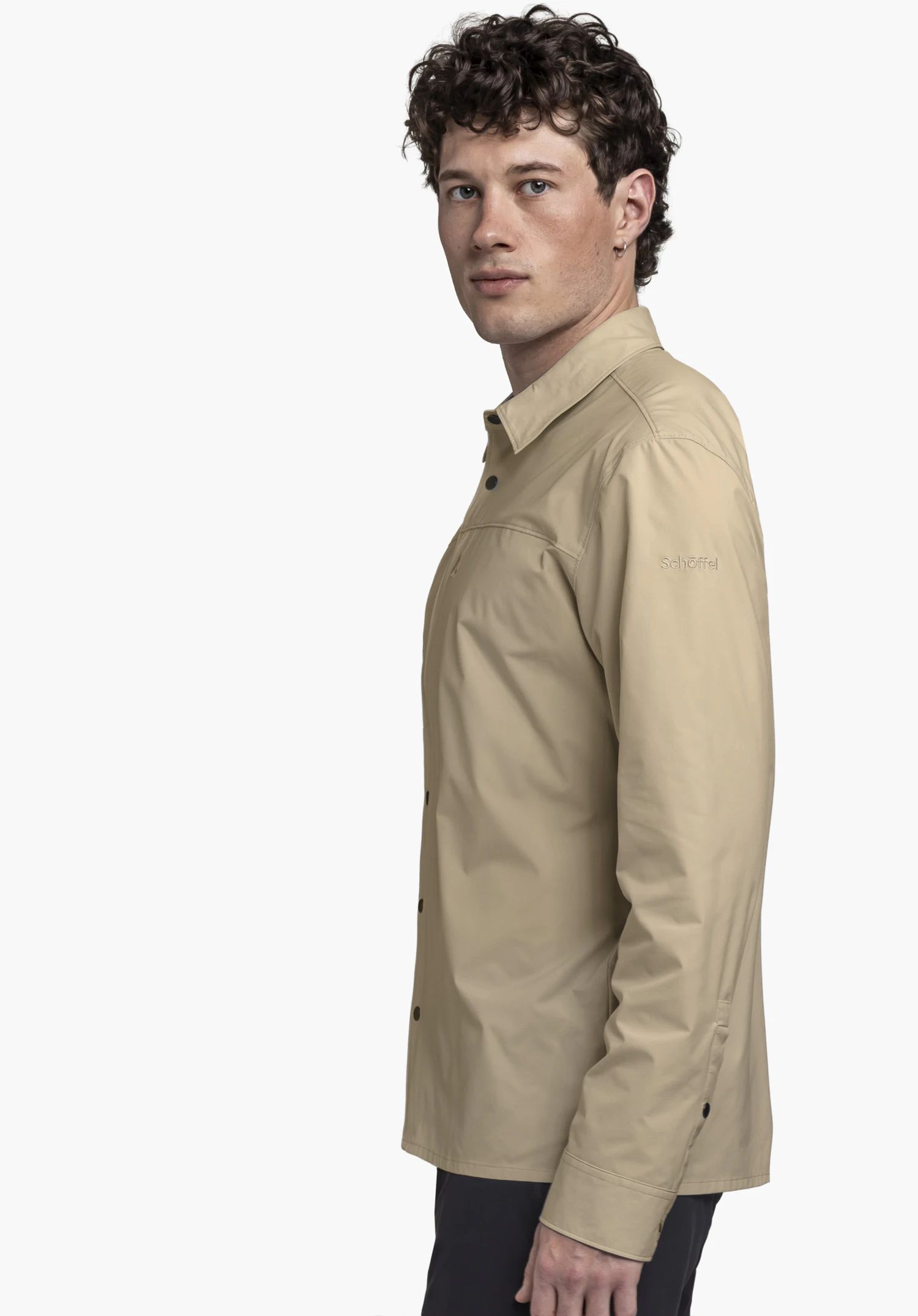 Shirt Style Maghera MEN in beige. The model stands sideways against a neutral background, looking directly at the camera. The clean design is perfectly complemented by the subtle Schöffel logo on the sleeve.