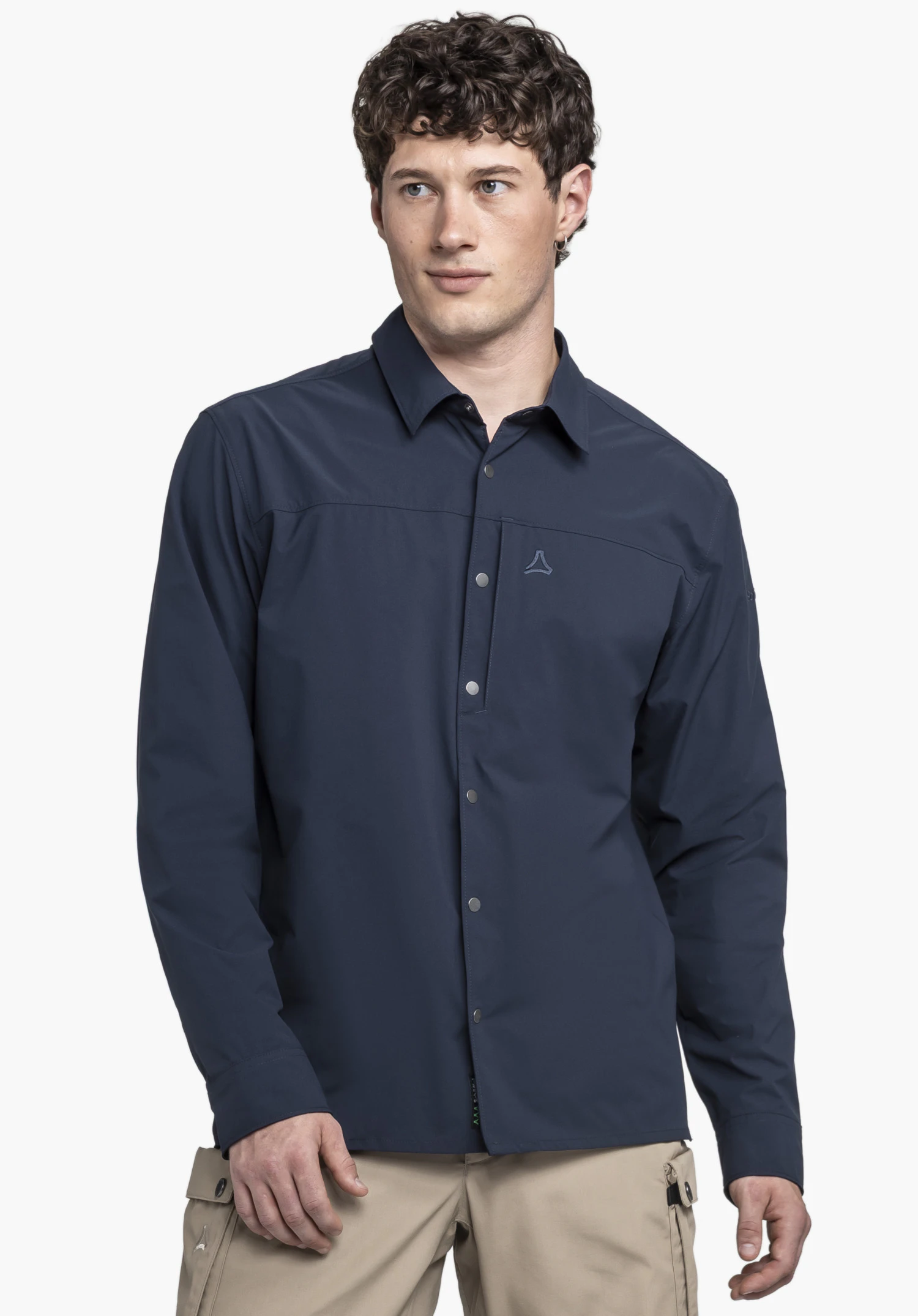 Shirt Style Maghera MEN. Un mannequin se tient de face et porte la chemise bleue à manches longues. Le logo Schöffel se trouve sur la poitrine gauche. La tenue est présentée sur un fond neutre.
