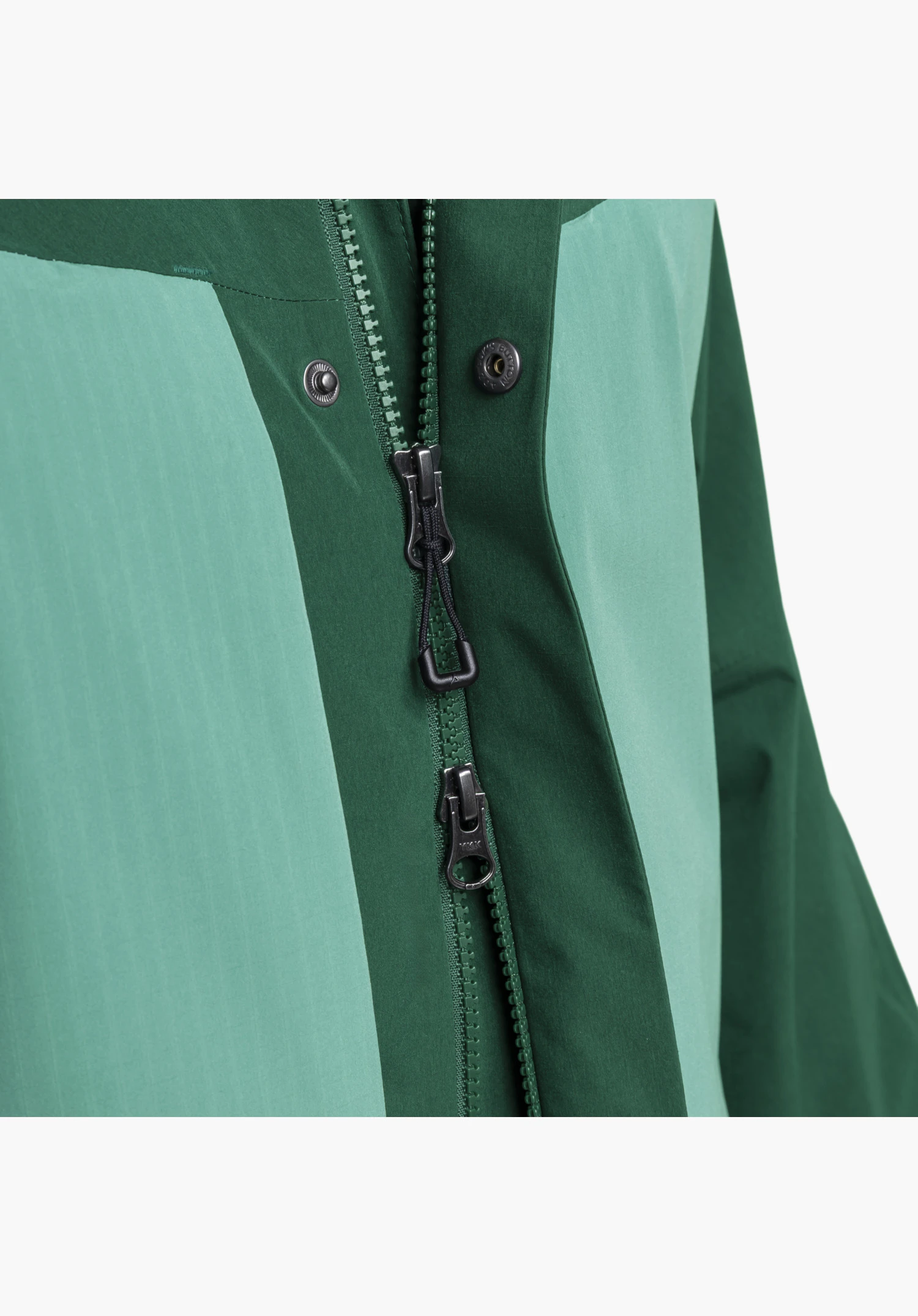 2L Jacket Style Maghera MEN zeigt den teilweise geöffneten Zwei-Wege-Reißverschluss und die Druckknöpfe der Abdeckleiste auf einem zweifarbigen grünen Stoff, Nahaufnahme vor weißem/neutralem Hintergrund.