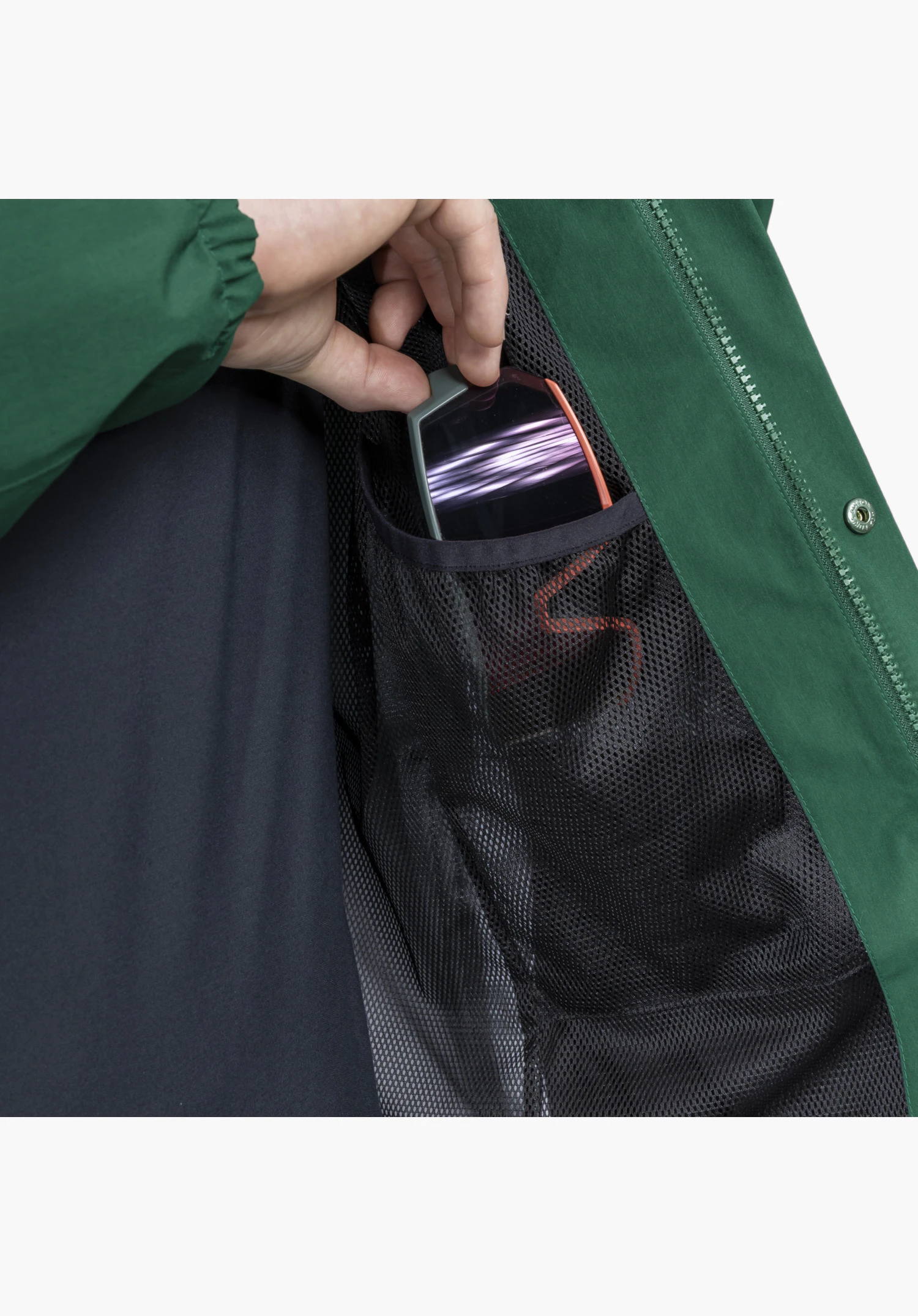 2L Jacket Style Maghera MEN zeigt eine praktische schwarze Netztasche im Inneren, aus der eine Hand eine Skibrille zieht, umrahmt von grünem Außenmaterial und einem Reißverschluss. Nahaufnahme vor weißem/neutralem Hintergrund.