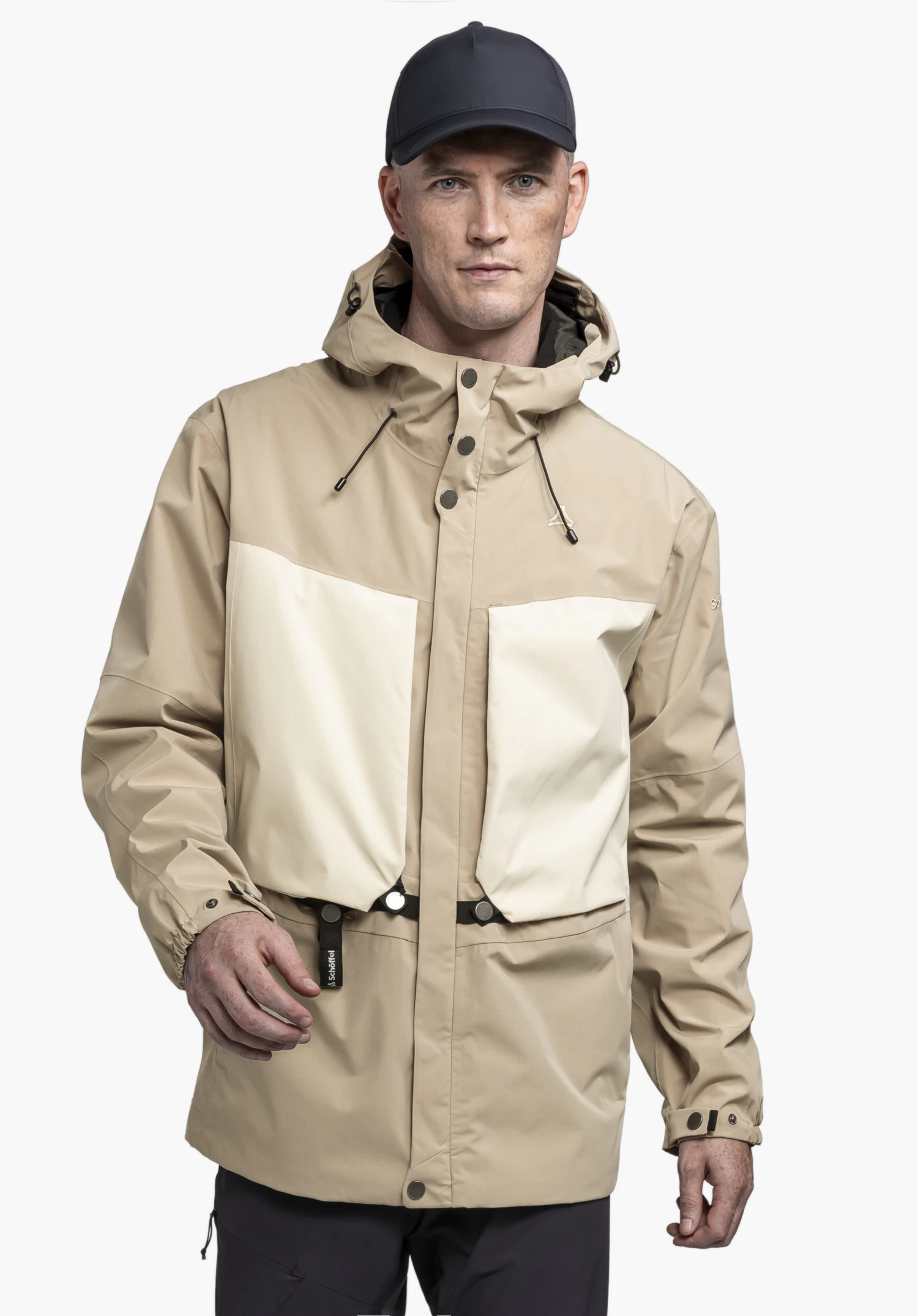 2L Jacket Style Maghera MEN worn by a model in the colour beige. The model stands frontally, presenting the jacket with colour-contrasting pockets and a visible Schöffel logo against a neutral background.