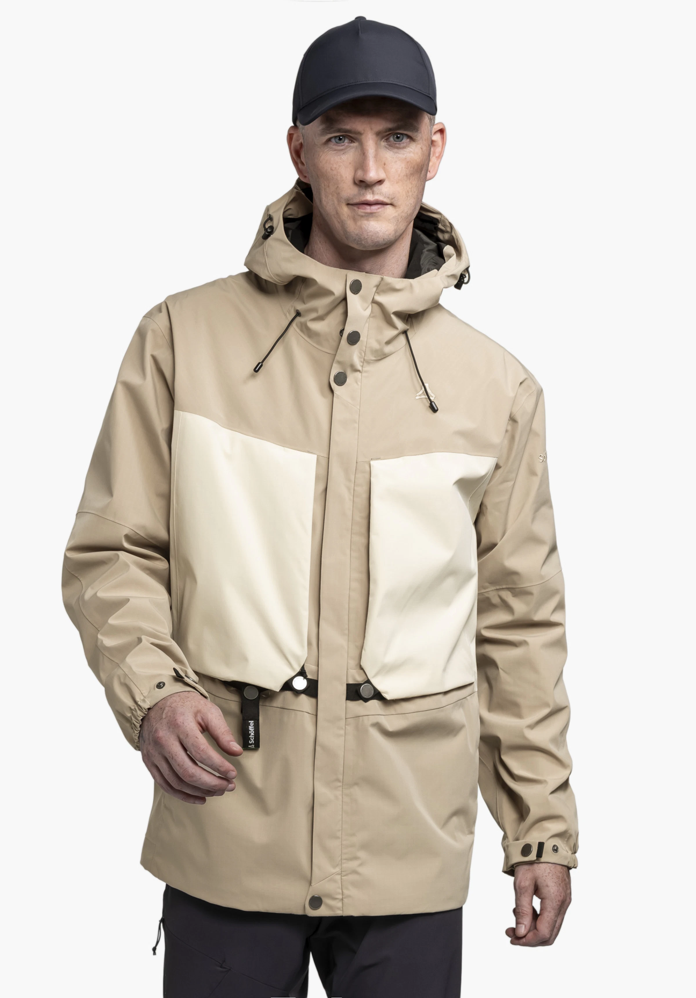 2L Jacket Style Maghera MEN worn by a model in the colour beige. The model stands frontally, presenting the jacket with colour-contrasting pockets and a visible Schöffel logo against a neutral background.
