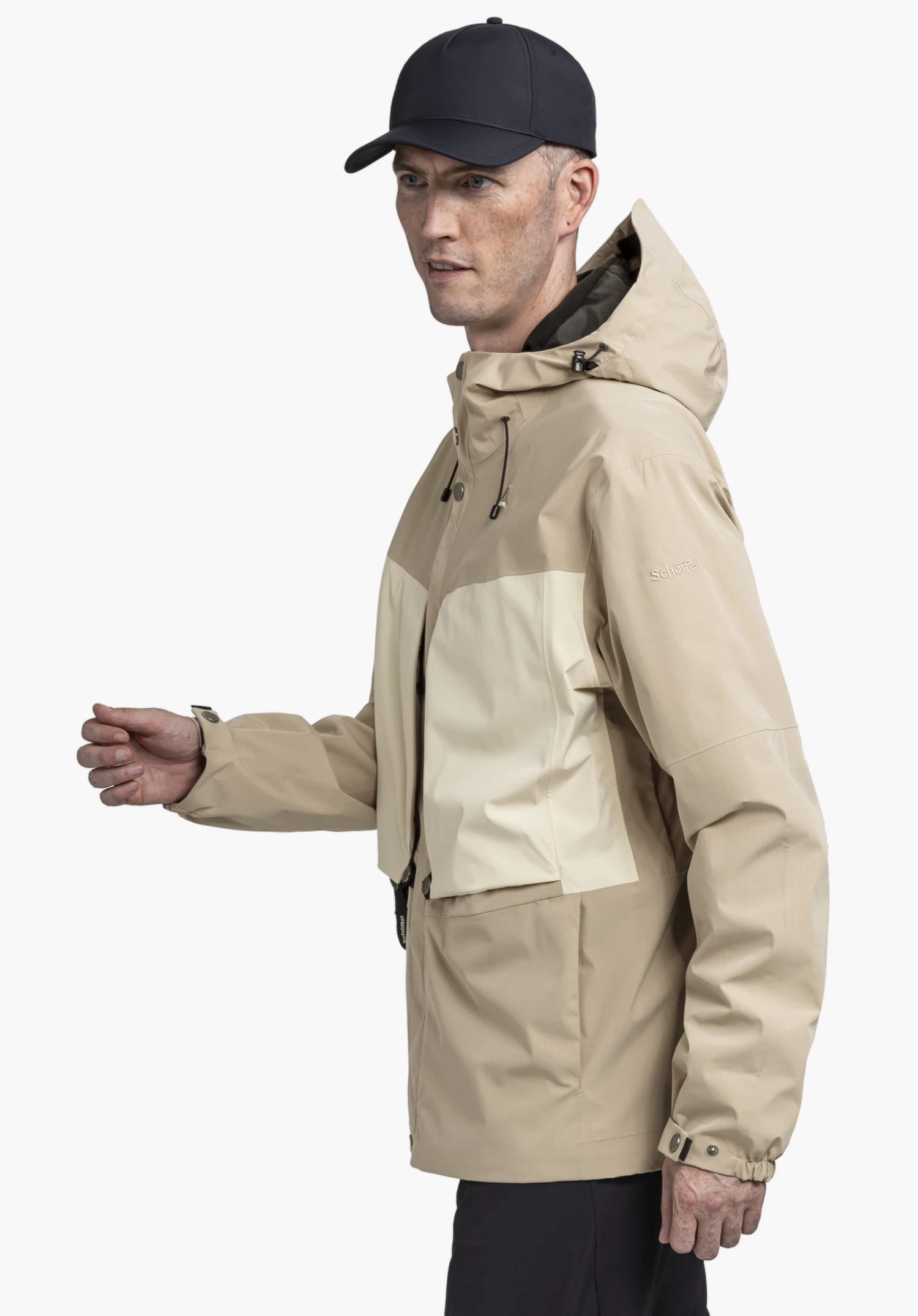 2L Jacket Style Maghera MEN in the colour beige shown against a neutral background. The model is standing in a slight side profile, wearing the jacket with the hood up. The subtle Schöffel logo is visible on the left upper arm.