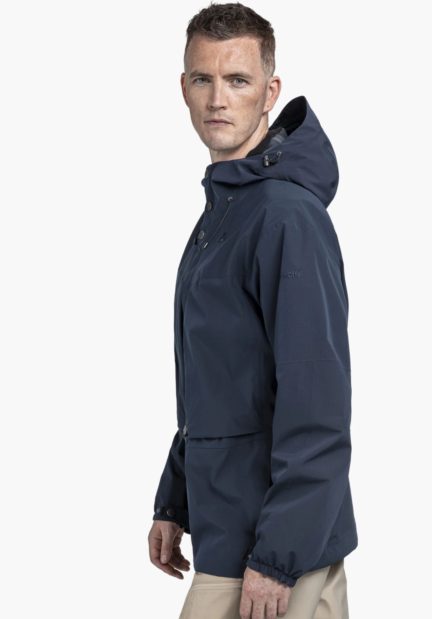 2L Jacket Style Maghera MEN in Blau. Der männliche Träger steht seitlich vor einem neutralen Hintergrund und blickt direkt in die Kamera. Das dezente Schöffel-Logo auf dem Oberarm ist gut zu erkennen.