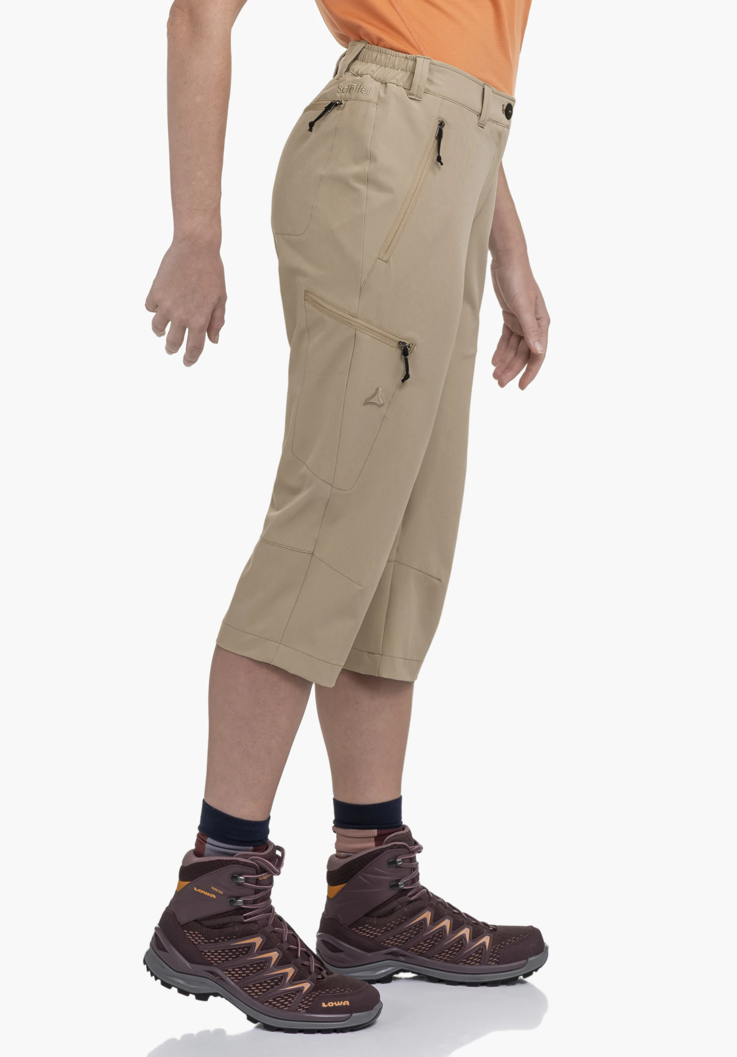 Pants Style Chavuma WMN wird von einem Model getragen, das seitlich steht. Die beigefarbene Hose zeigt praktische Reißverschlusstaschen und das Schöffel-Logo auf dem Oberschenkel in einer Trageansicht vor einem neutralen Hintergrund.