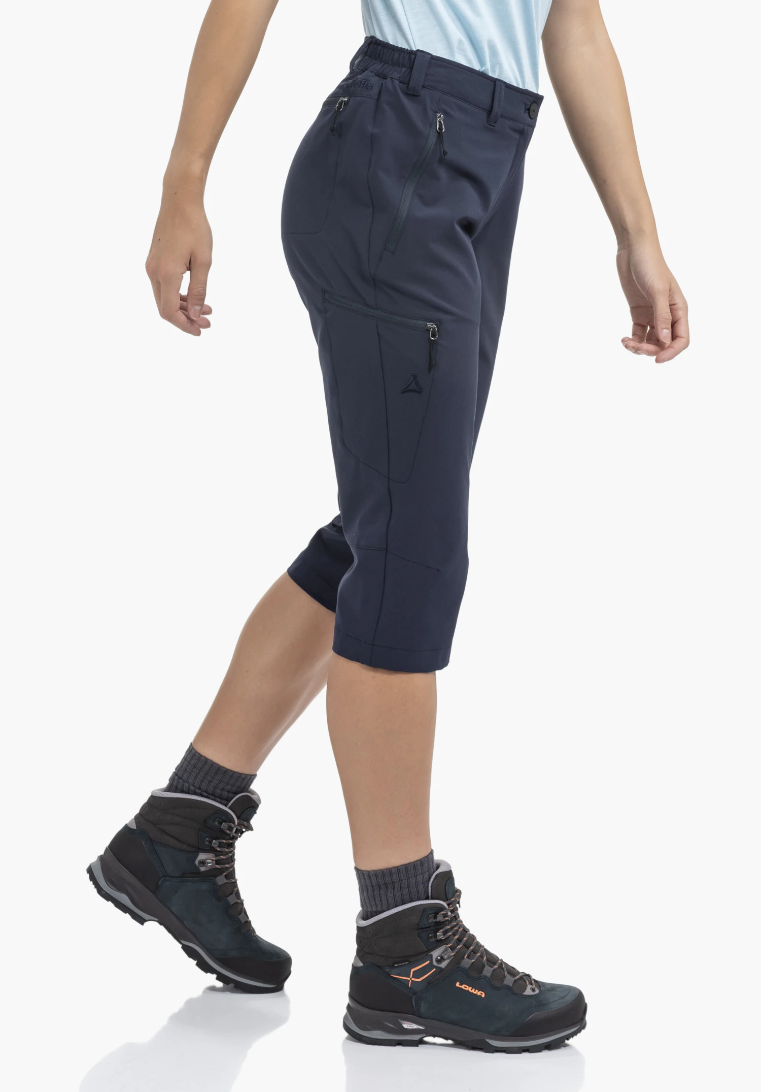 Pants Style Chavuma WMN in Blau wird von einem Model getragen, das seitlich steht. Neben Reißverschlusstaschen ist das Schöffel-Logo auf dem seitlichen Bein sichtbar, fotografiert vor einem neutralen Hintergrund.