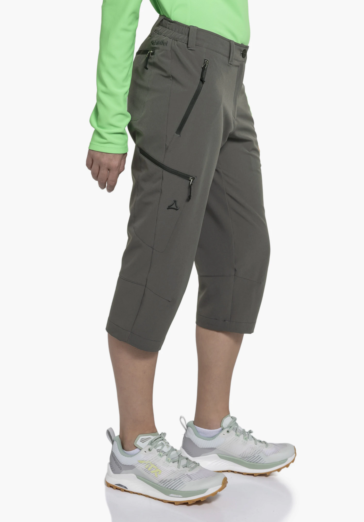 Pants Style Chavuma WMN als graue 3/4-Hose an einem Model, das seitlich steht und Details wie Reißverschlusstaschen sowie das Schöffel-Logo am Bund und Bein zeigt, vor einem neutralen Hintergrund.