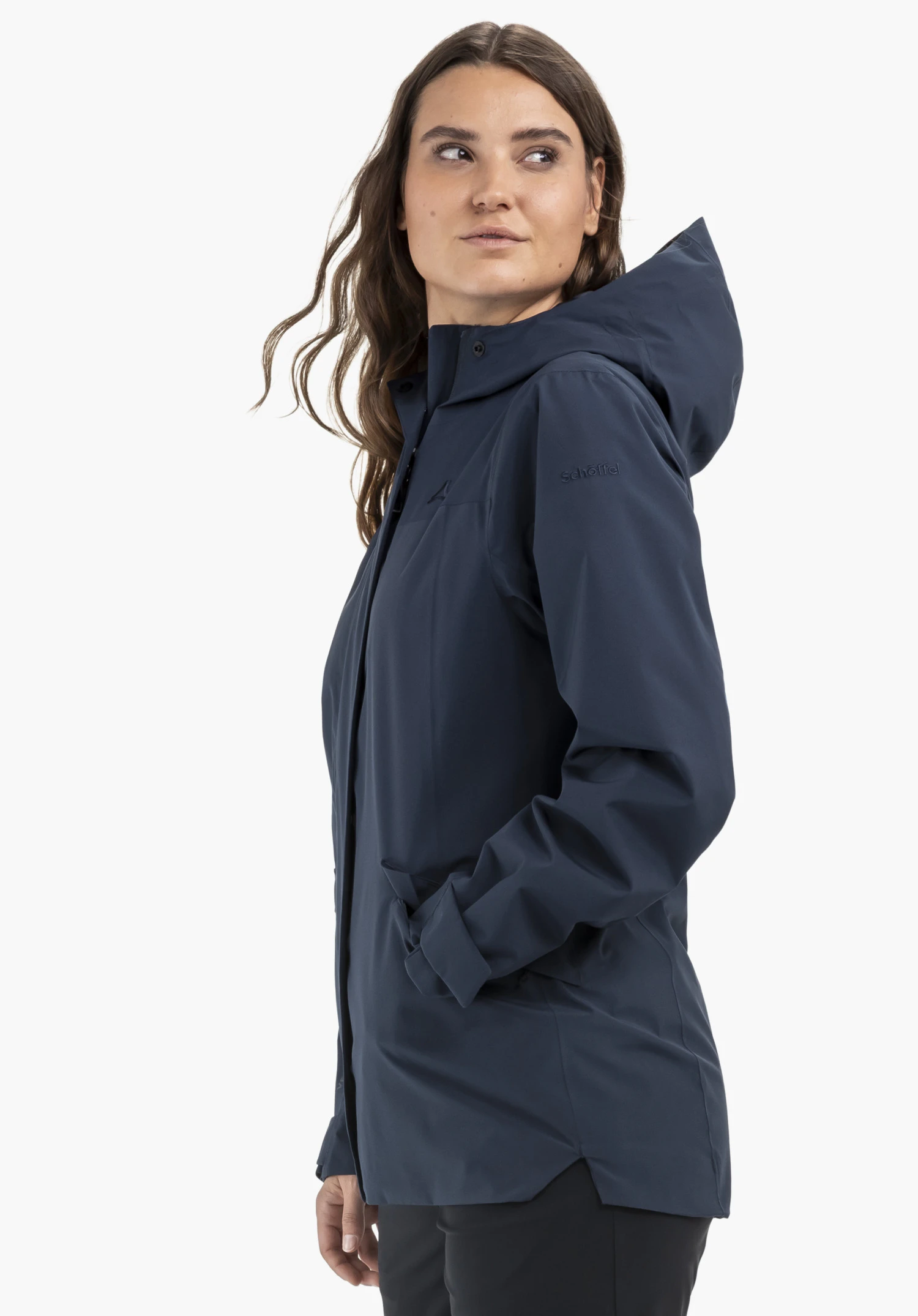 CIRC Jacket Style Smue WMN. Das Model trägt die Jacke in Blau und steht seitlich mit einer Hand in der Tasche. Am linken Oberarm ist das Schöffel-Logo sichtbar, fotografiert vor einem neutralen Hintergrund.