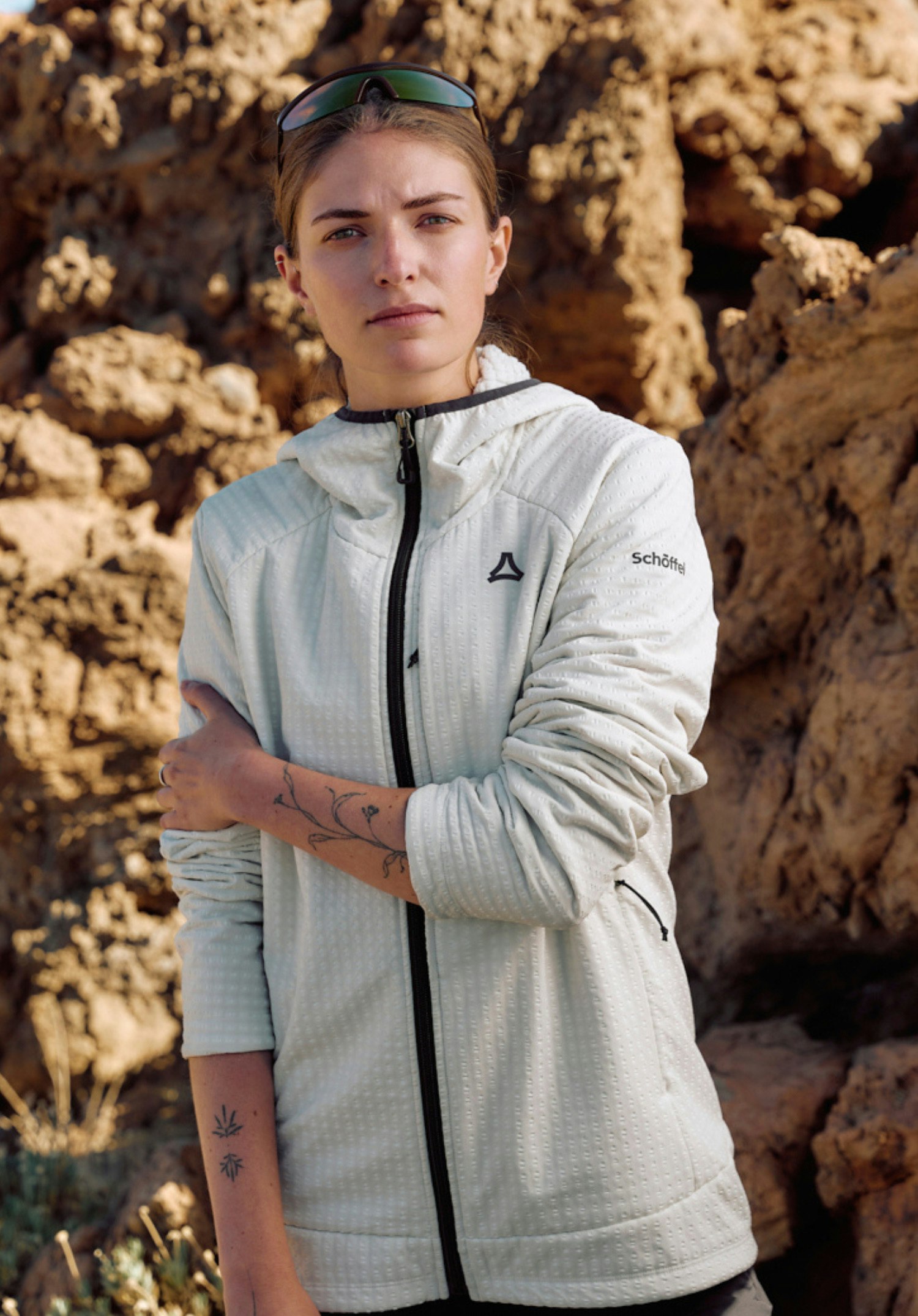 Fleece Hoody Style Enixa WMN in the colour natur on a model. The woman stands frontally, looking directly at the camera with one hand casually in her side pocket, while the dark Schöffel-Logo stands out on the left chest area, presented against a neutral background.