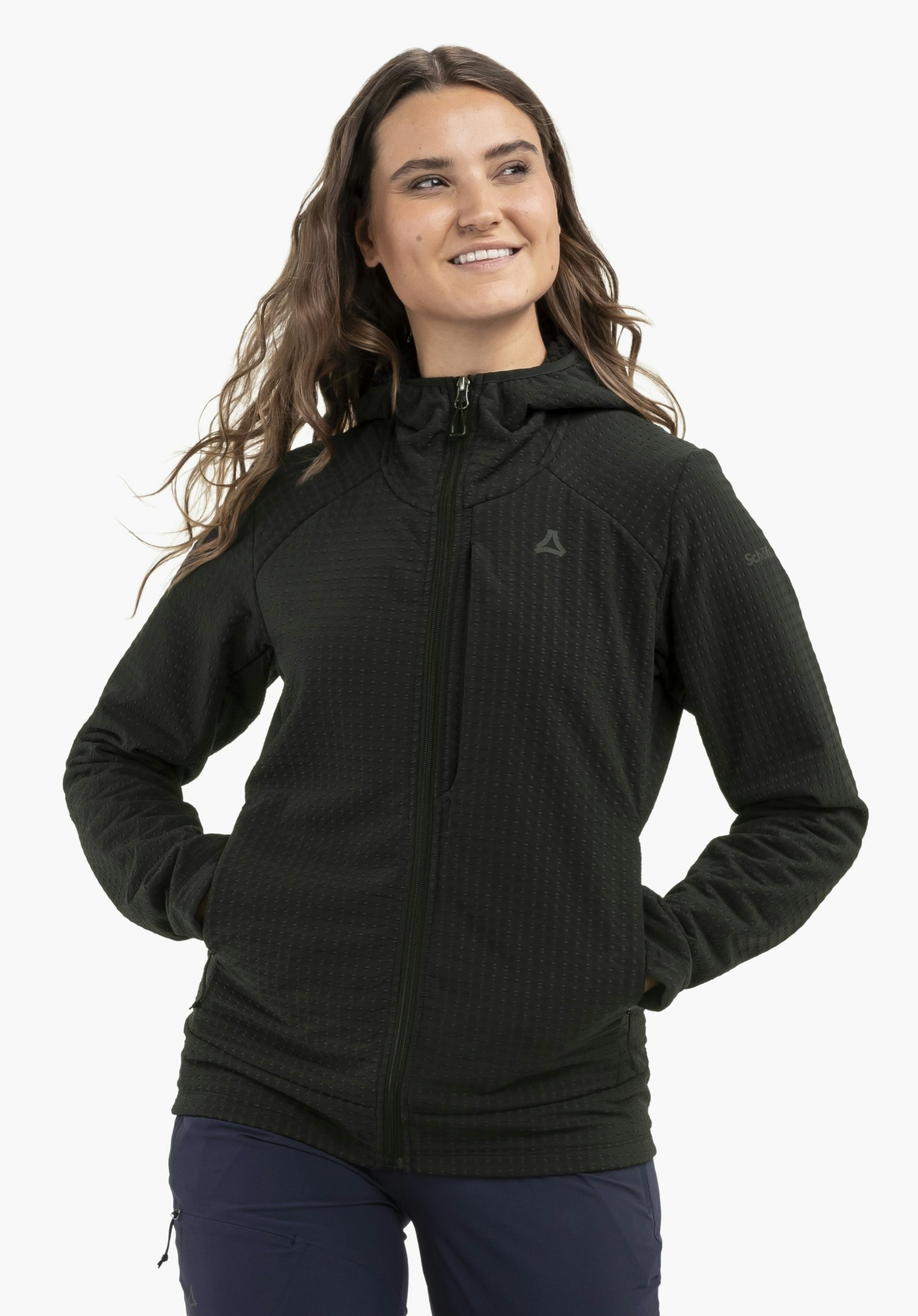 Fleece Hoody Style Enixa WMN porté par un mannequin qui se tient de face, sourit et garde les mains dans les poches. Le sweat à capuche noir est orné du logo Schöffel sur la poitrine gauche et est présenté devant un fond neutre.