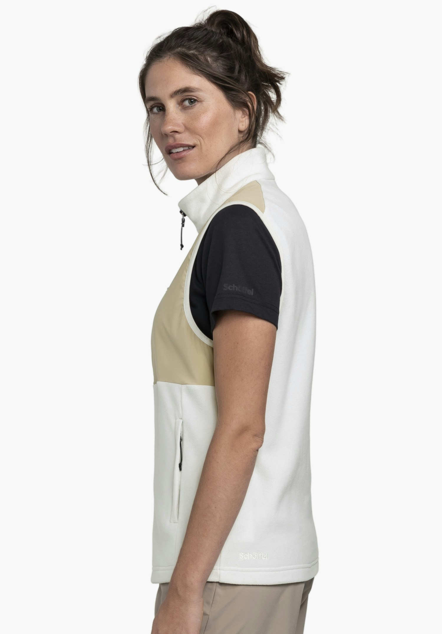 Fleece Vt Style Ash WMN an einem Model, das seitlich steht. Man sieht die Fleeceweste in der Farbe Natur mit farblich abgesetzten Einsätzen an der Brust und einem sichtbaren Schöffel-Logo am unteren Saum vor einem neutralen Hintergrund.
