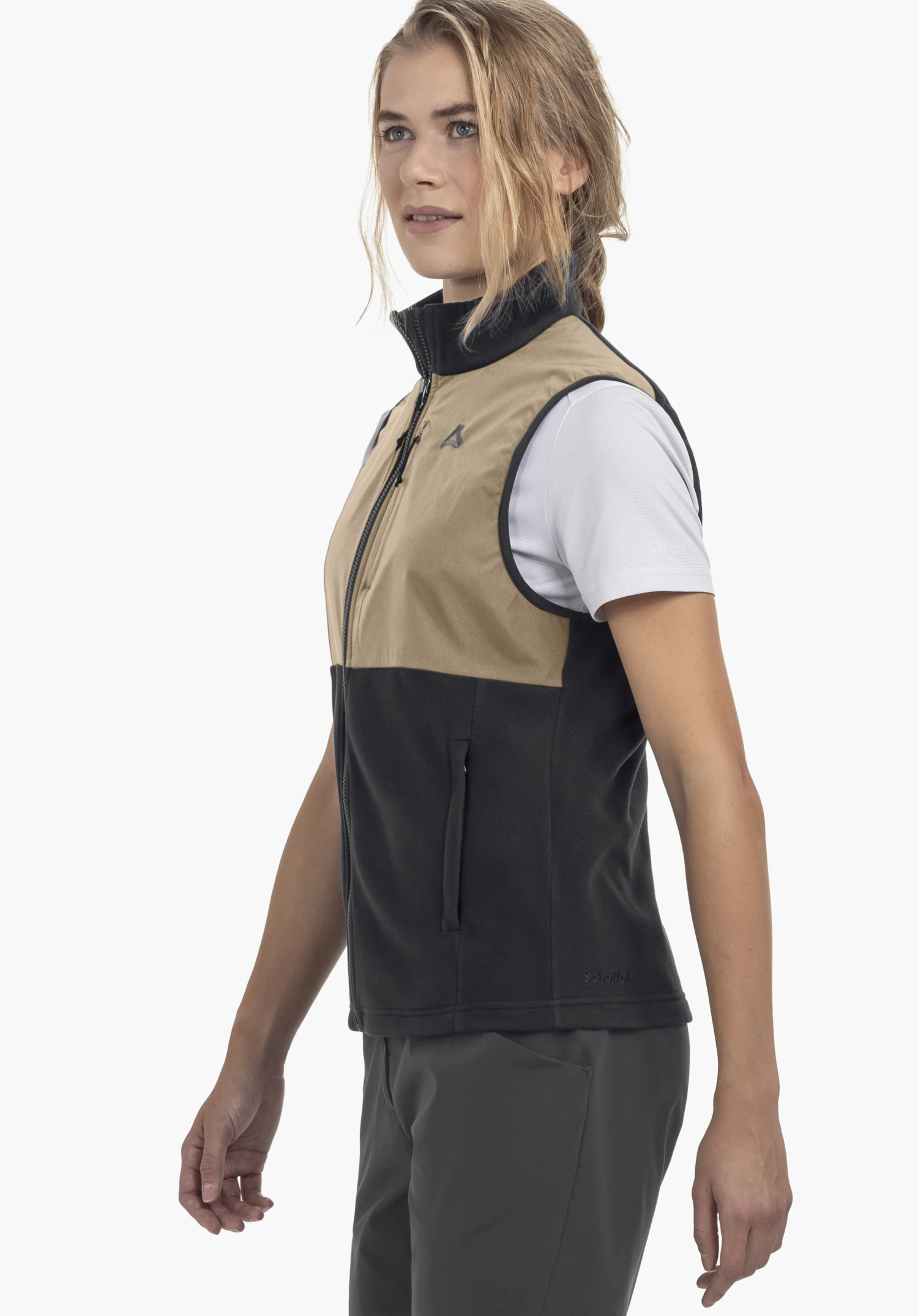 Fleece Vt Style Ash WMN gedragen door een model dat zijwaarts staat. Het vest in zwart is voorzien van een doorlopende ritssluiting, een contrasterend schoudergedeelte en het Schöffel-logo op de linkerborst tegen een neutrale achtergrond.