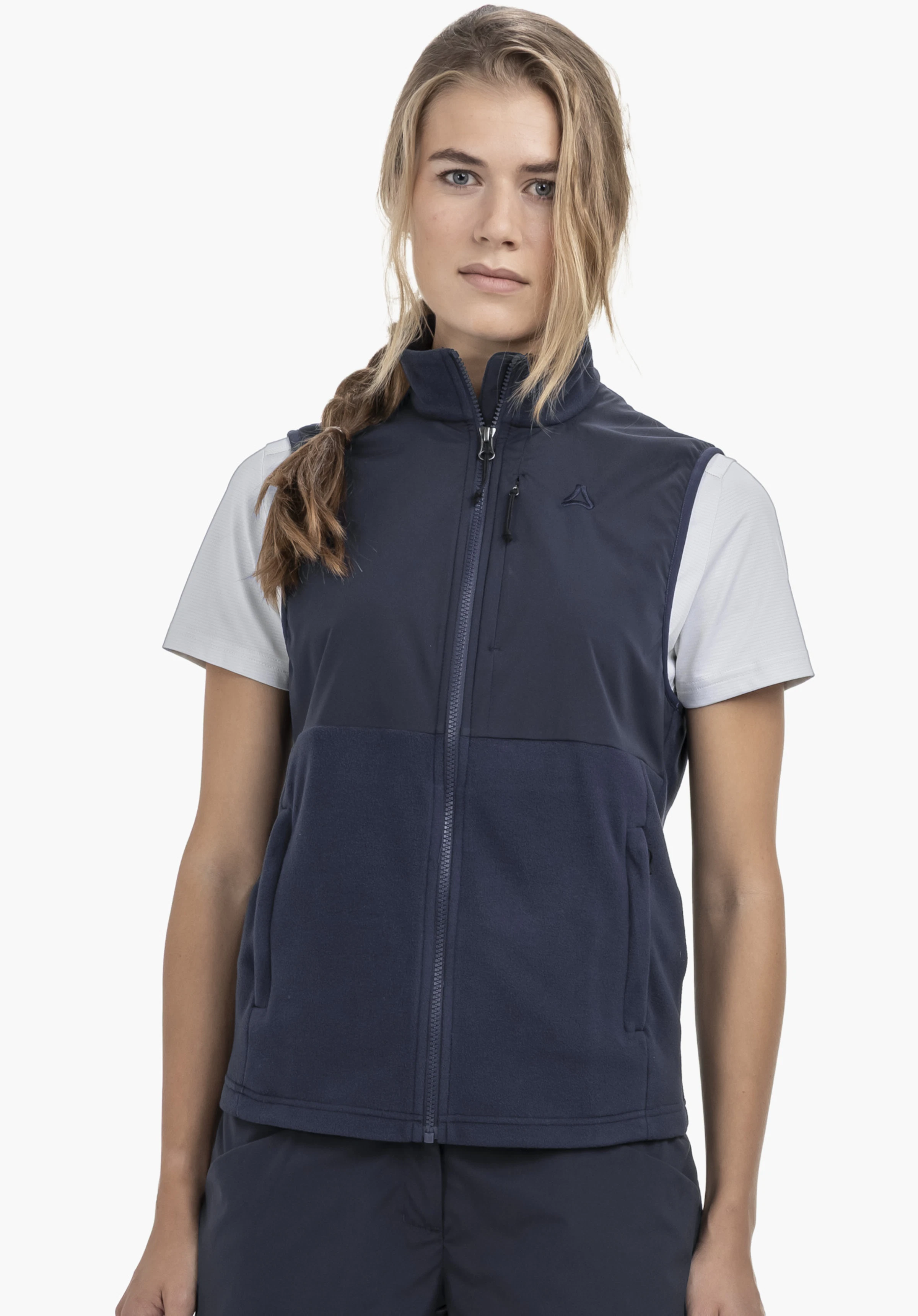 Fleece Vt Style Ash WMN getragen von einem Model, das frontal steht und in die Kamera blickt. Sie präsentiert die blaue Weste mit sichtbarem Schöffel-Logo auf der linken Brust vor einem neutralen Hintergrund.