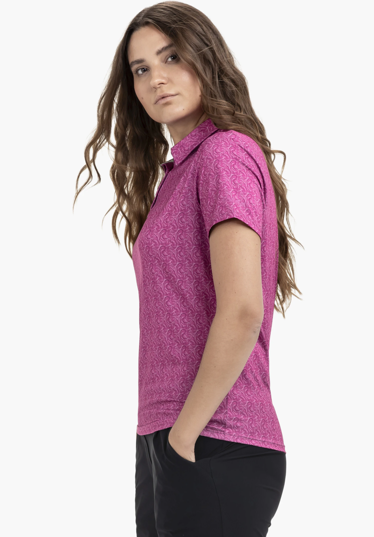 Polo Shirt Style Fraydo WMN in kräftigem Pink. Das Model steht seitlich zum Betrachter und blickt direkt in die Kamera. Vor einem neutralen Hintergrund kommt das auffällige Muster des Poloshirts optimal zur Geltung.