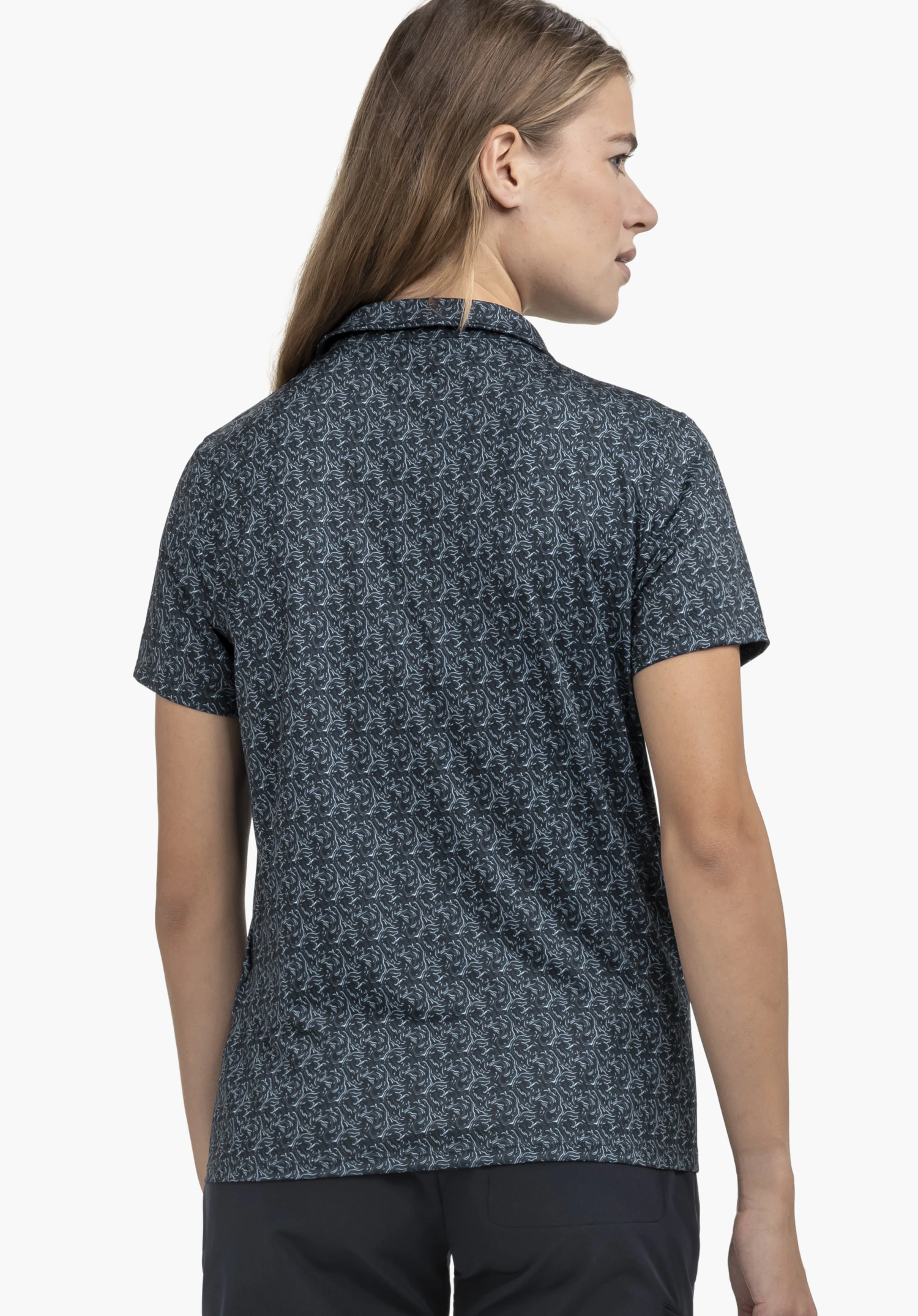 Polo Shirt Style Fraydo WMN in Blau mit vollflächigem Muster, präsentiert an einem Model in der Rückenansicht. Das Model steht vor einem neutralen Hintergrund und blickt zur Seite.