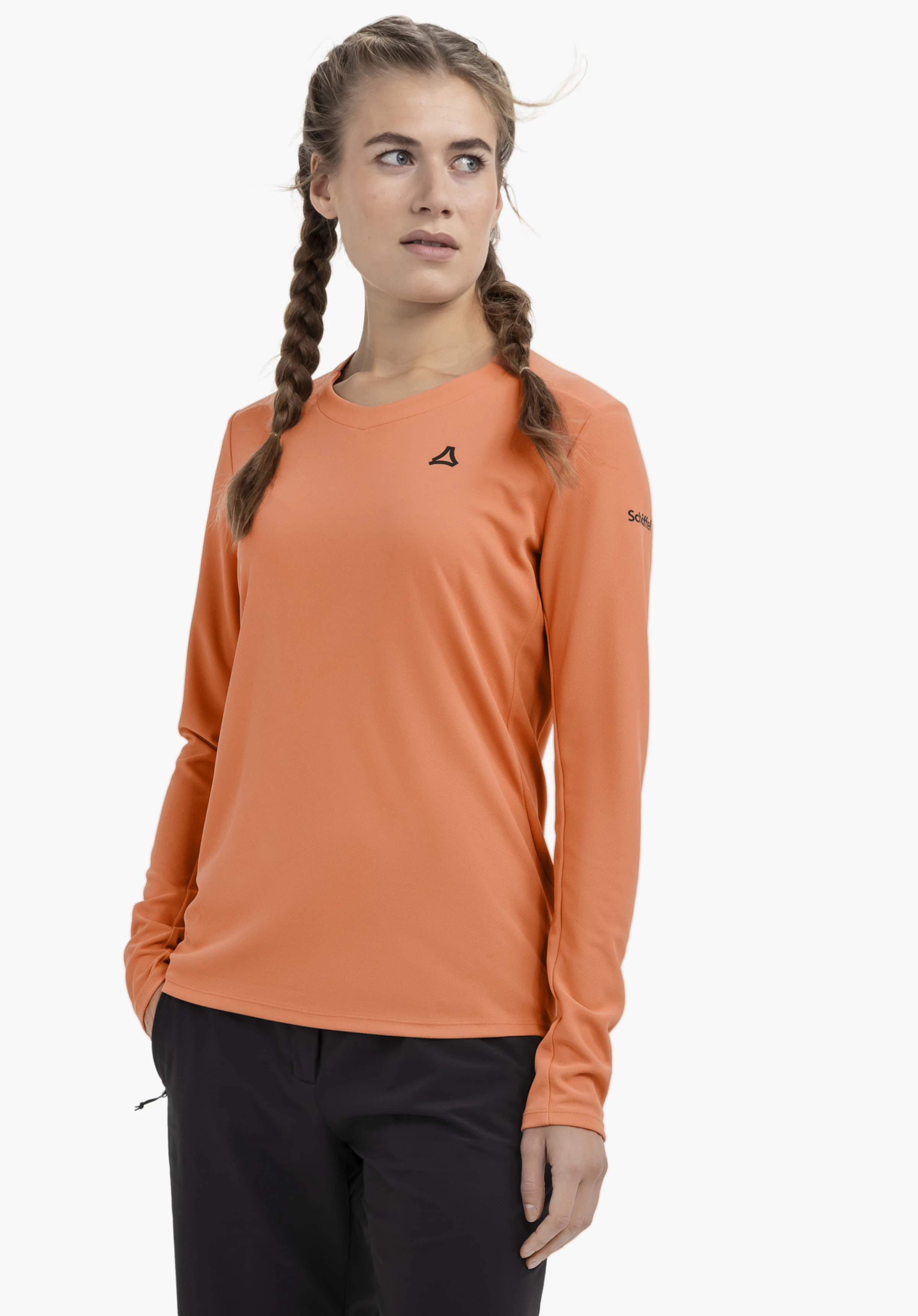 Longsleeve Style Enixa WMN de couleur orange, porté par un mannequin. Le mannequin se tient légèrement de profil, présentant ce haut à manches longues avec le logo Schöffel bien visible sur la poitrine et la manche devant un fond neutre.