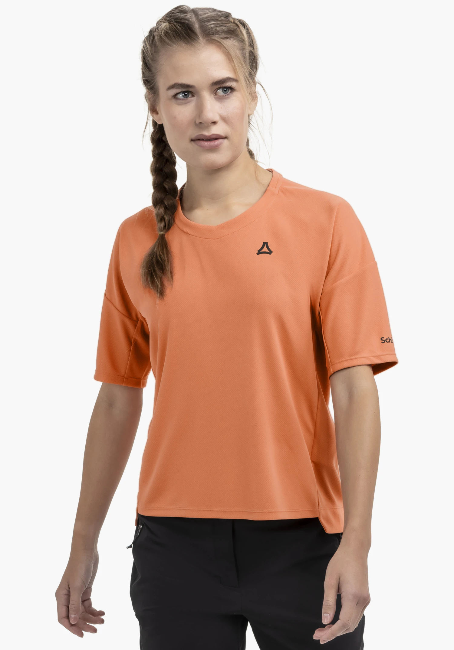 T Shirt Style Enixa WMN. Ein Model steht frontal und trägt das orange Shirt mit dem Schöffel-Logo auf der Brust vor einem neutralen Hintergrund.