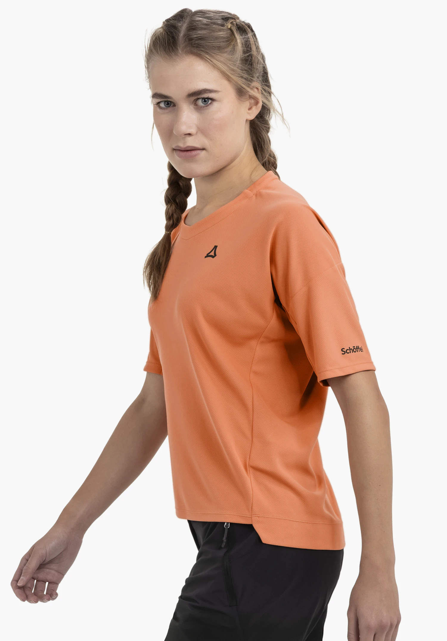 T Shirt Style Enixa WMN in vibrant orange. The model is captured in a side profile against a neutral background while walking. The subtle Schöffel logo is clearly visible on the chest and the sleeve.