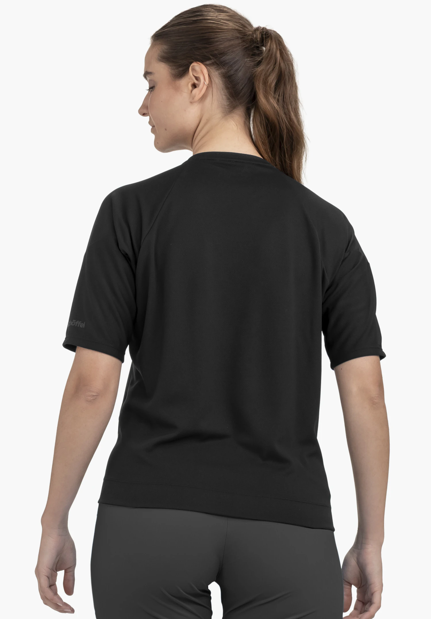 T Shirt Style Enixa WMN in the colour black. The model is shown from the back, looking slightly over her left shoulder, and the Schöffel logo is visible on the left sleeve. The image presents the top against a neutral background.