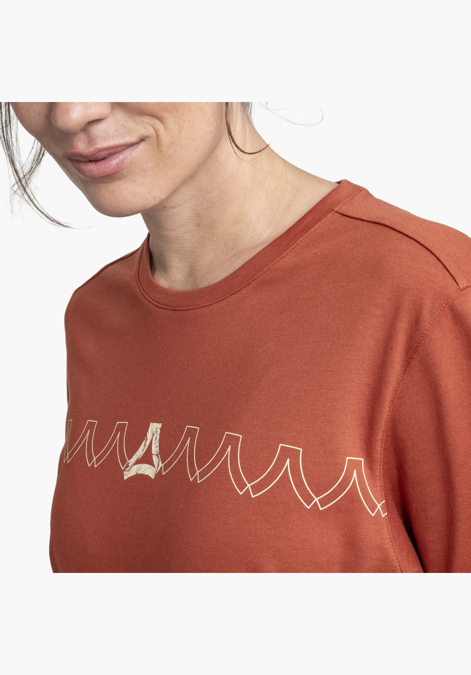 T Shirt Style Elmori WMN worn by a model in a close-up, standing slightly turned to the side. The red shirt features a graphic zig-zag print on the chest, photographed against a neutral background.