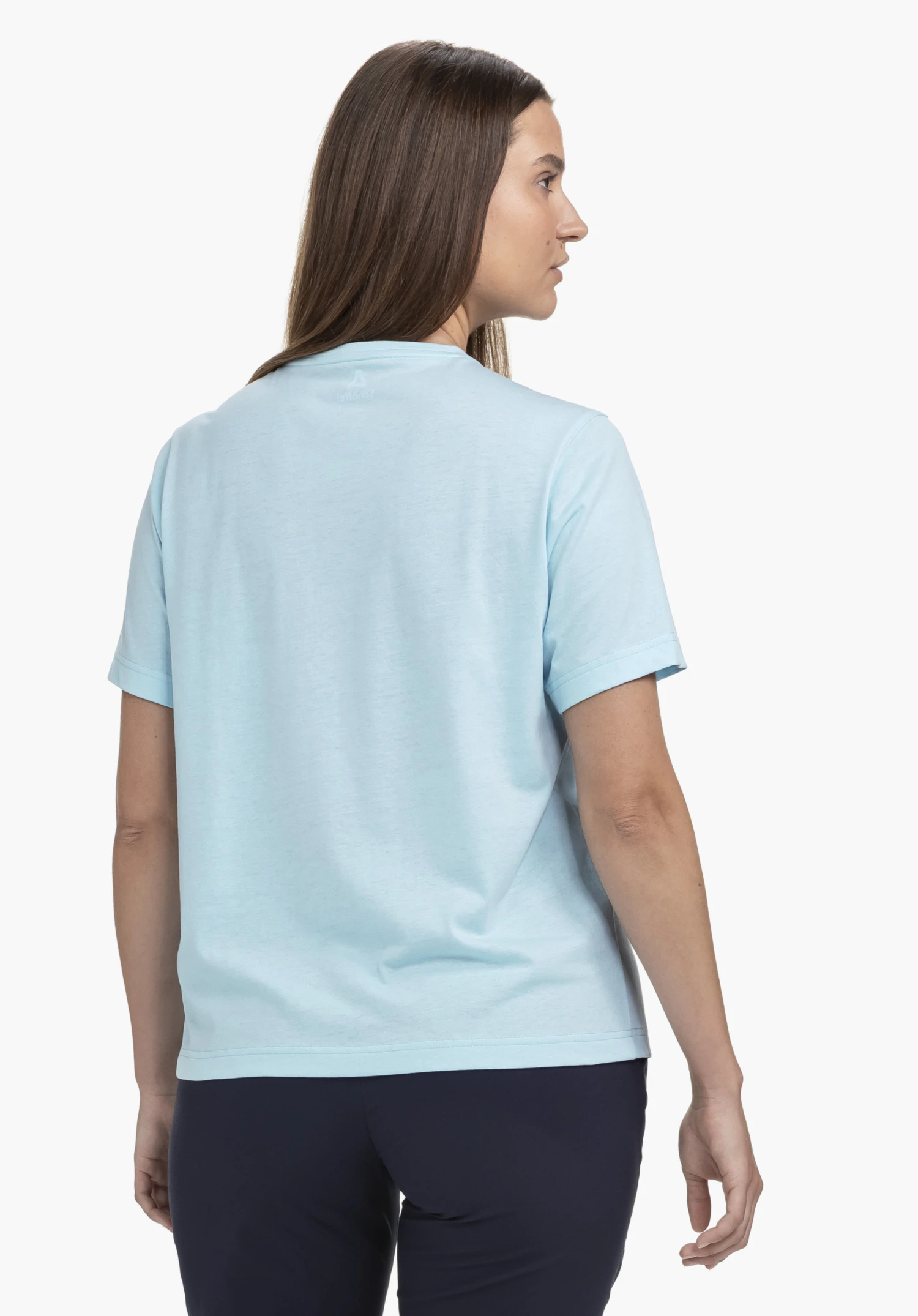T Shirt Style Elmori WMN en bleu. Le mannequin est vu de dos et se tient légèrement de profil, avec un petit logo Schöffel visible au niveau de la nuque. Le t-shirt est présenté sur un fond neutre.