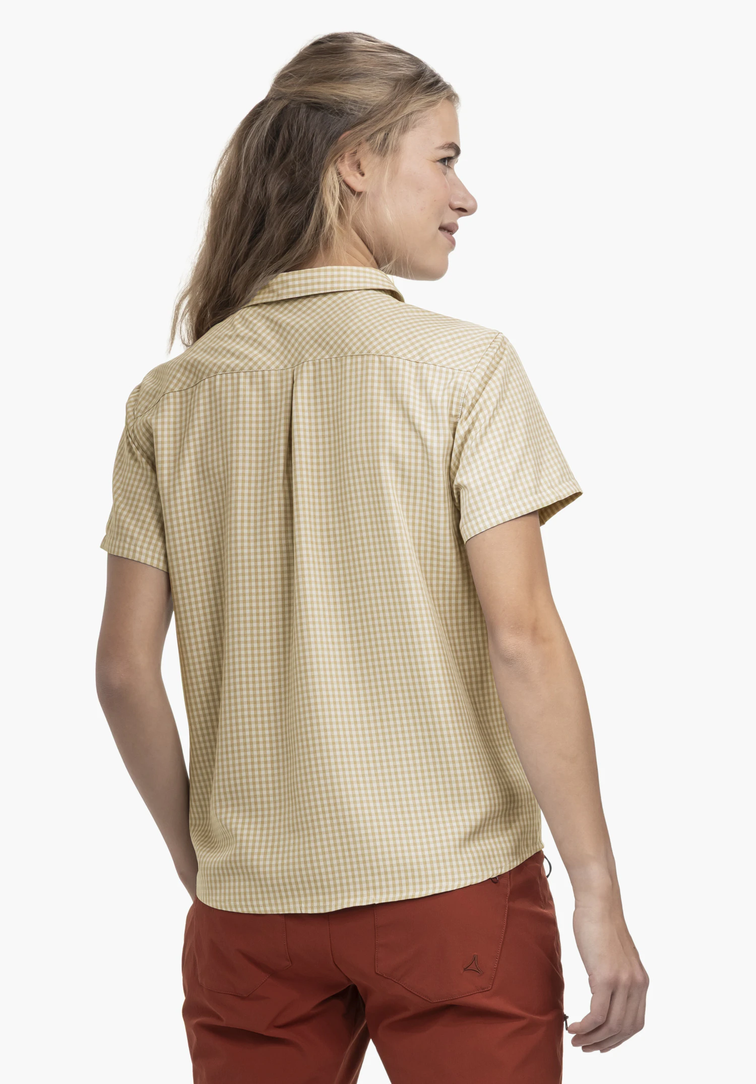 CIRC Blouse Style Dalfoss WMN : Une jeune femme présente le chemisier dans le coloris natur de dos devant un fond neutre. Cette vue met en évidence la coupe classique et le motif à carreaux du chemisier, tandis que le discret logo Schöffel est visible sur le pantalon rouge foncé.