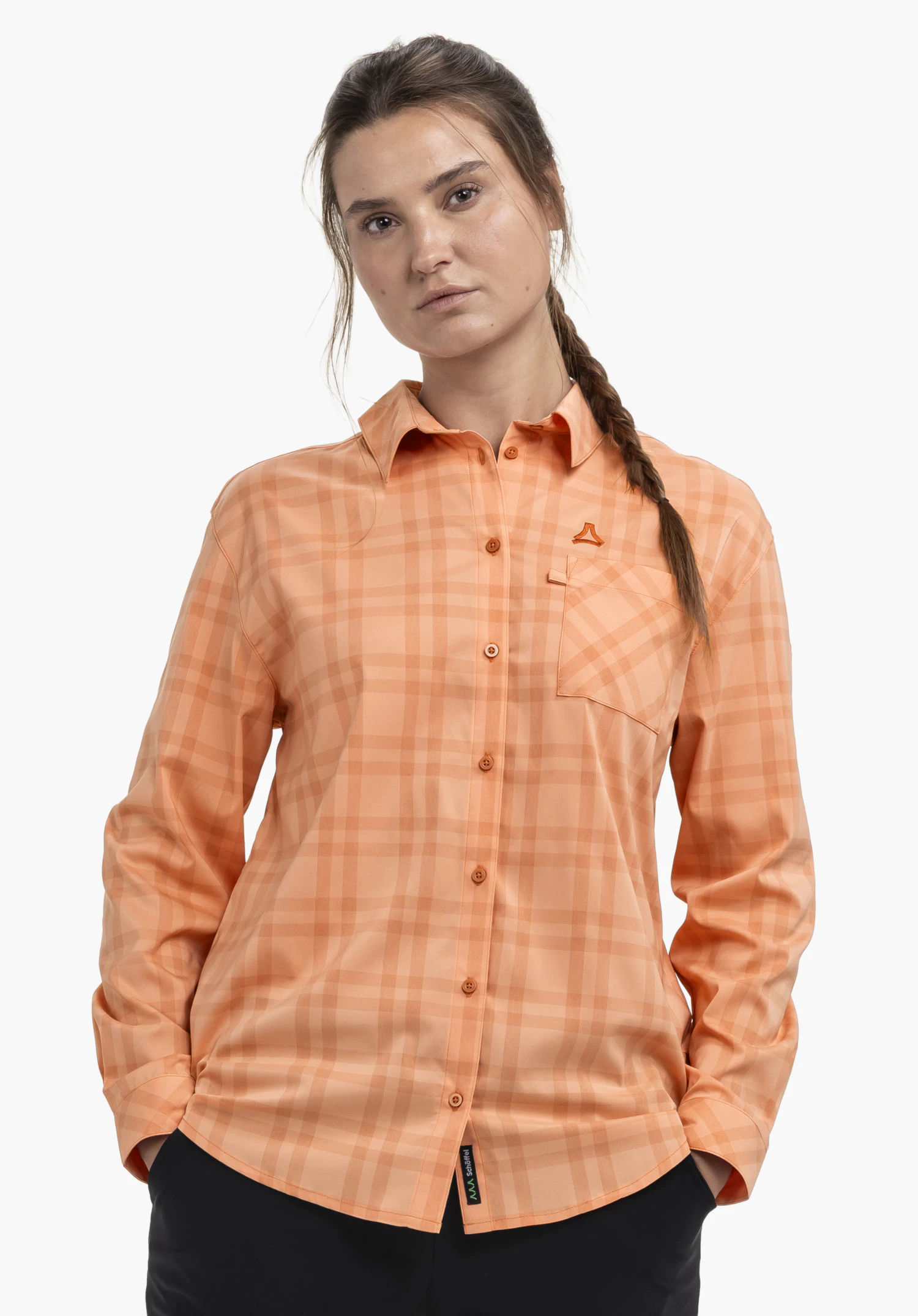 Blouse Style Fraris WMN. Ein Model trägt die orangefarbene Bluse und steht frontal mit den Händen in den Hosentaschen. Das Schöffel-Logo ist über der linken Brusttasche sichtbar. Das Ganze wird vor einem neutralen Hintergrund präsentiert.