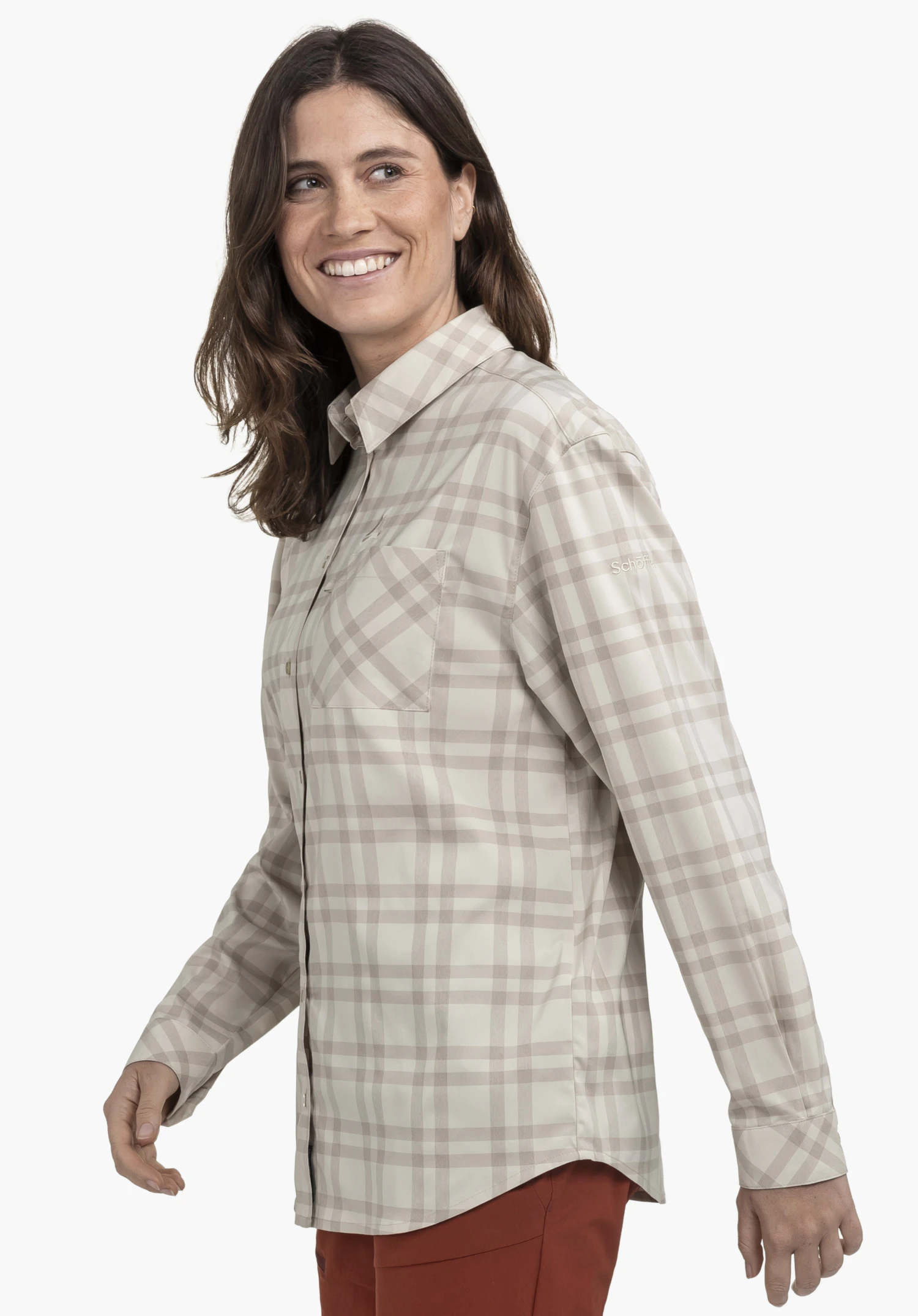 Blouse Style Fraris WMN portée par un mannequin qui se tient de profil et sourit. Le chemisier à carreaux en beige présente un logo Schöffel discret sur la manche gauche et est présenté sur un fond neutre.