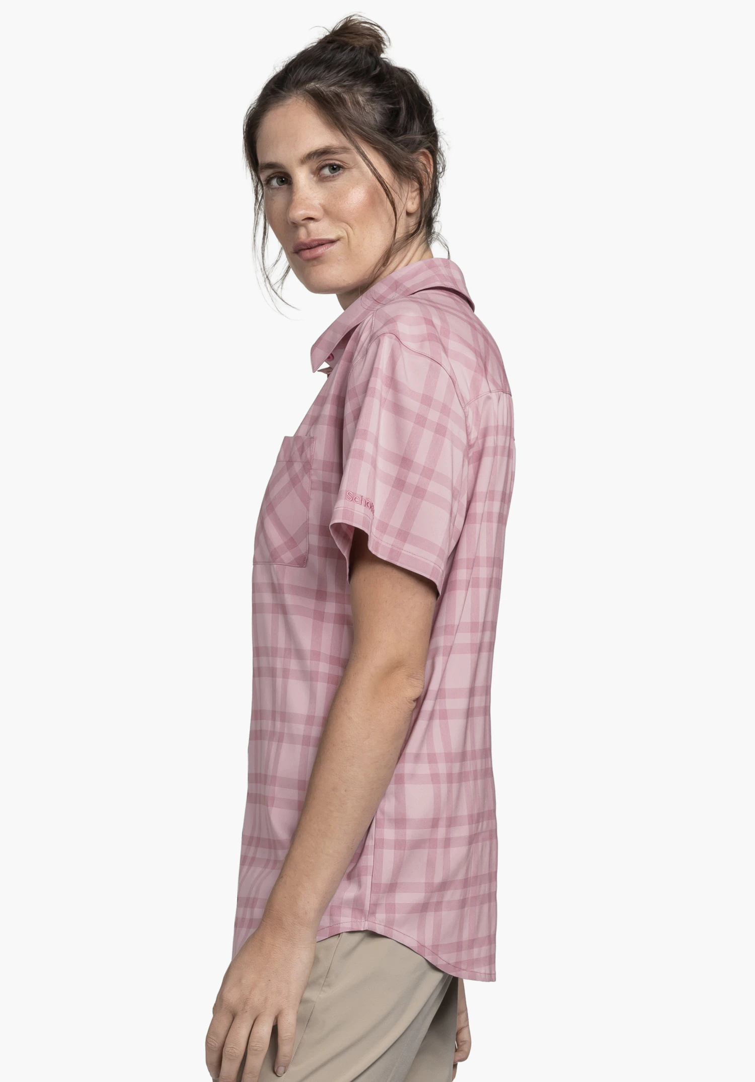 Blouse Style Frolya WMN wird von einem Model getragen, das seitlich steht. Die rosa karierte Kurzarmbluse zeigt das Schöffel-Logo auf dem Ärmel, fotografiert vor einem neutralen Hintergrund.