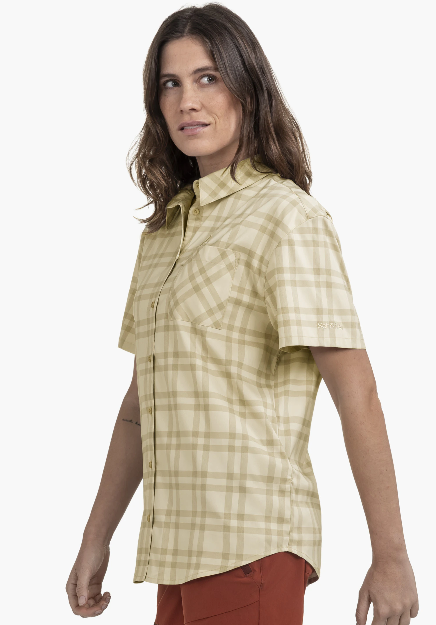 Blouse Style Frolya WMN getragen von einem Model, das seitlich steht. Die karierte, beigefarbene Kurzarmbluse zeigt eine Brusttasche und das Schöffel-Logo auf dem linken Ärmel und wird vor einem neutralen Hintergrund präsentiert.